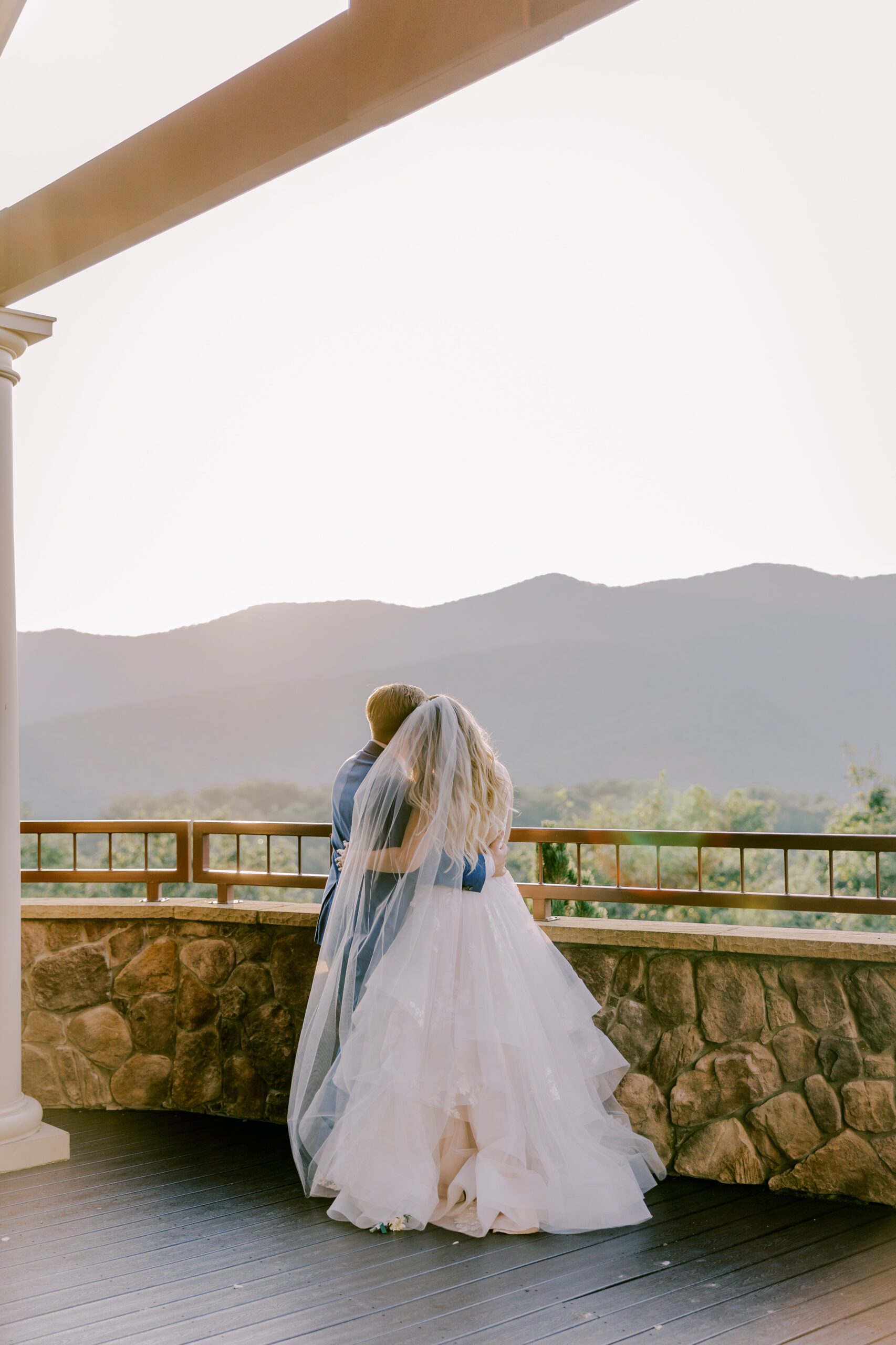 Bride and groom with their arms around one another as they look out at the mountains