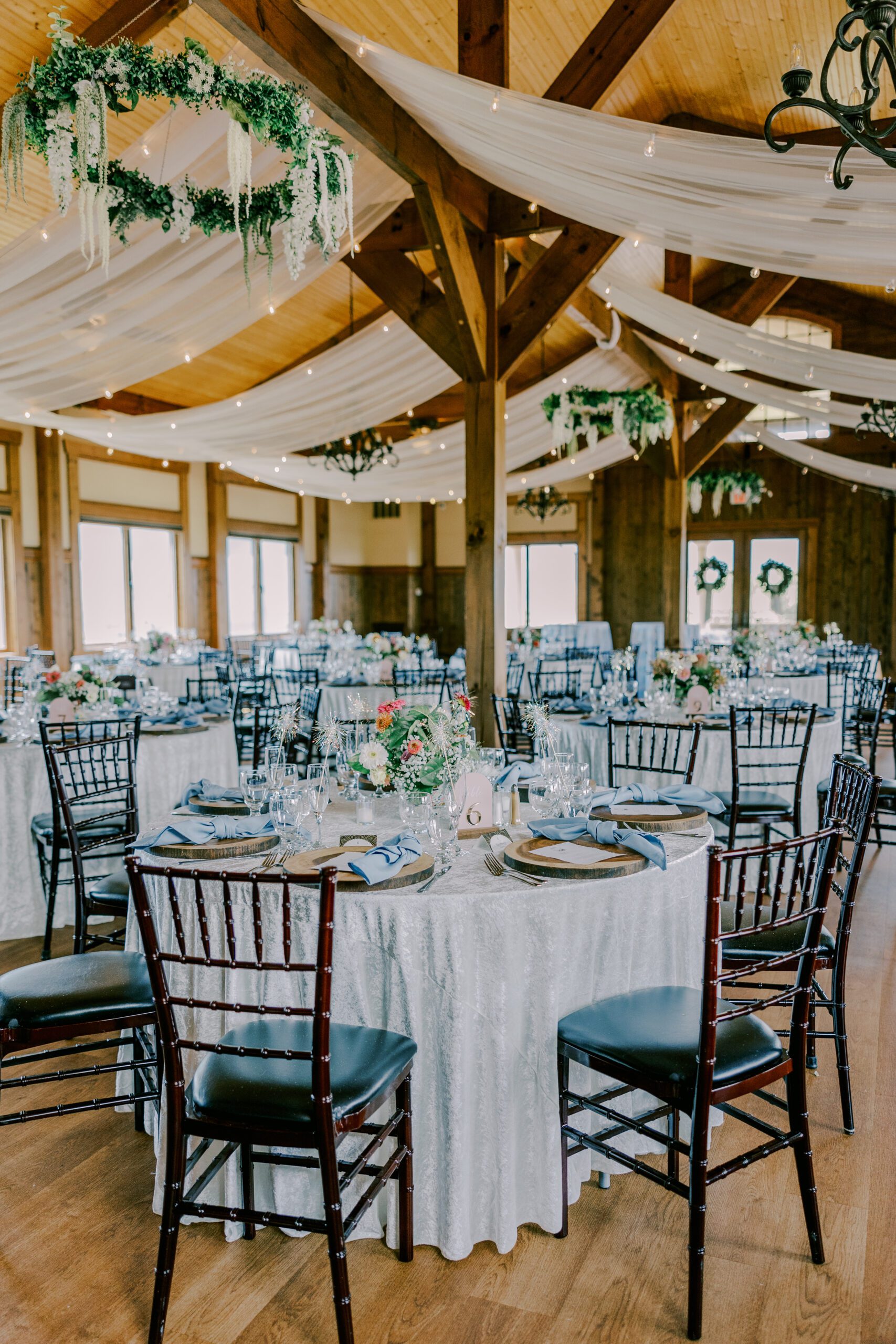 Tables set up in the reception space at irvine estate, white material is draped from the ceiling and circles of greenery and floral chandaliers