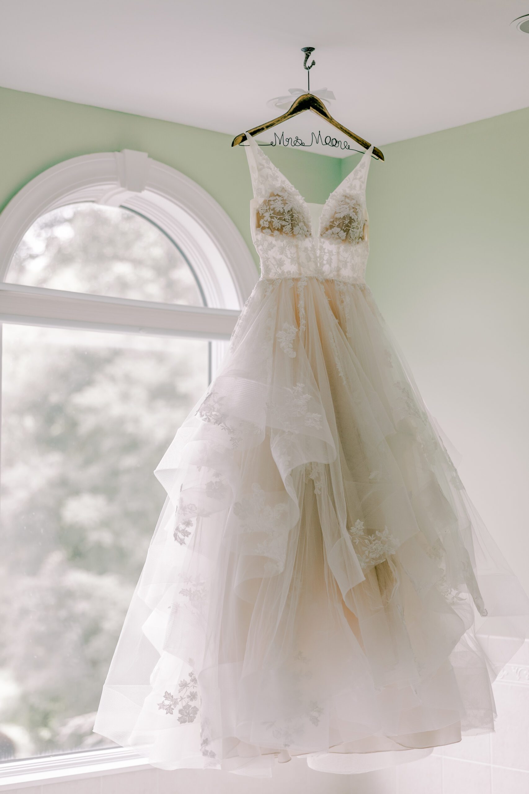 Wedding dress hanging from ceiling in front of a window at irvine estate