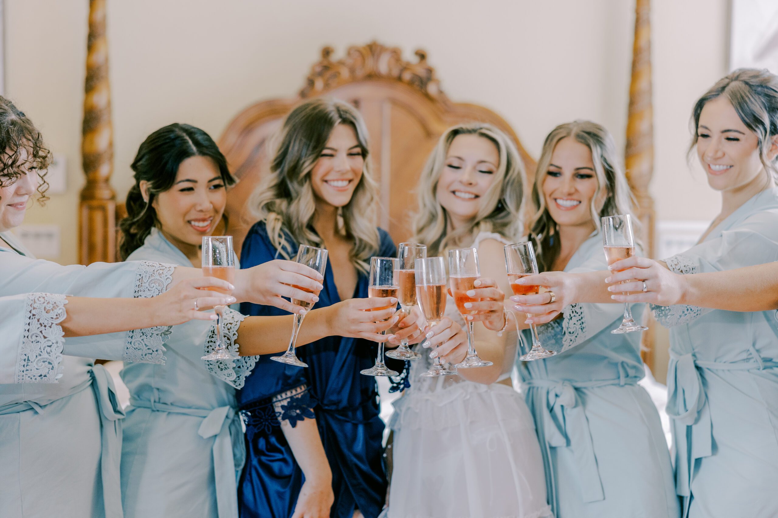 Bride and bridesmaids toasting a pink beverage. Bride in a little white dress and bridesmaids all in blue robes