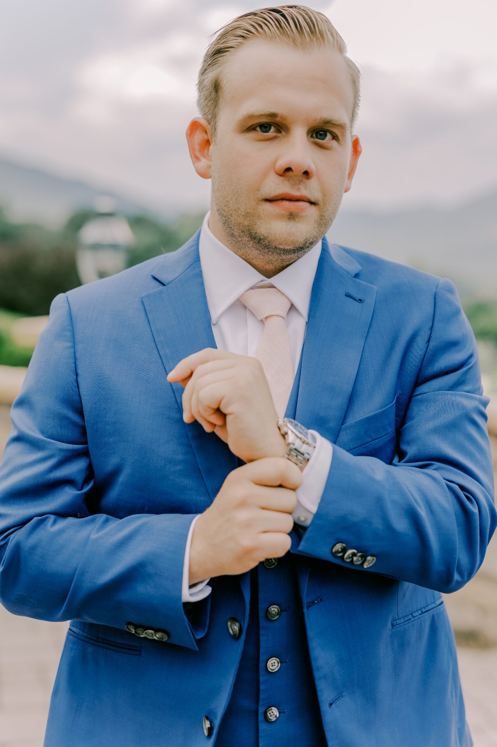 Groom in a blue suit adjusting his watch and looking at camera at irvine estate