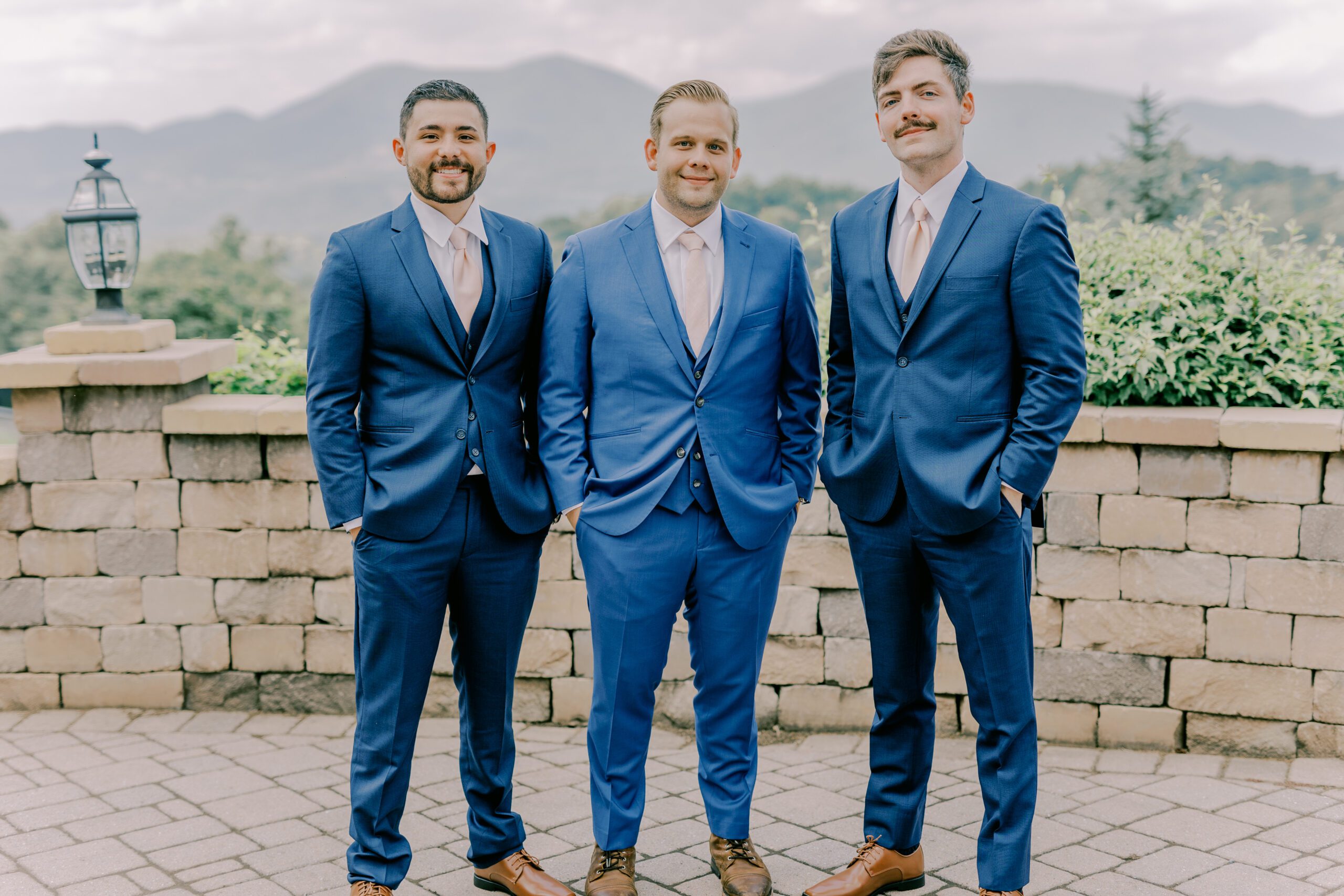 Groom and two groomsmen stand in matching blue suits smiling at camera.