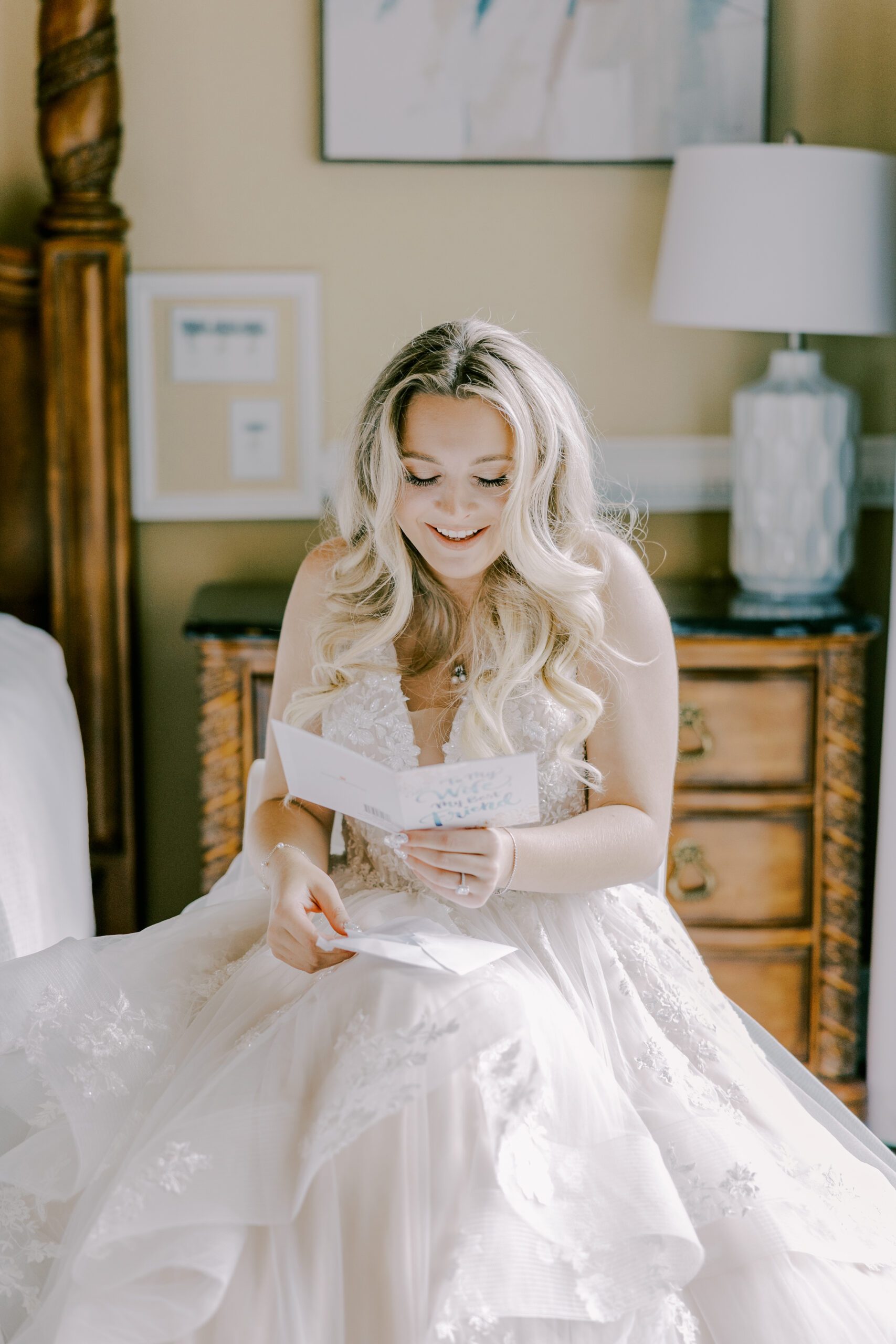 Bride sitting in her wedding dress, reading a card and smiling down at it at irvine estate