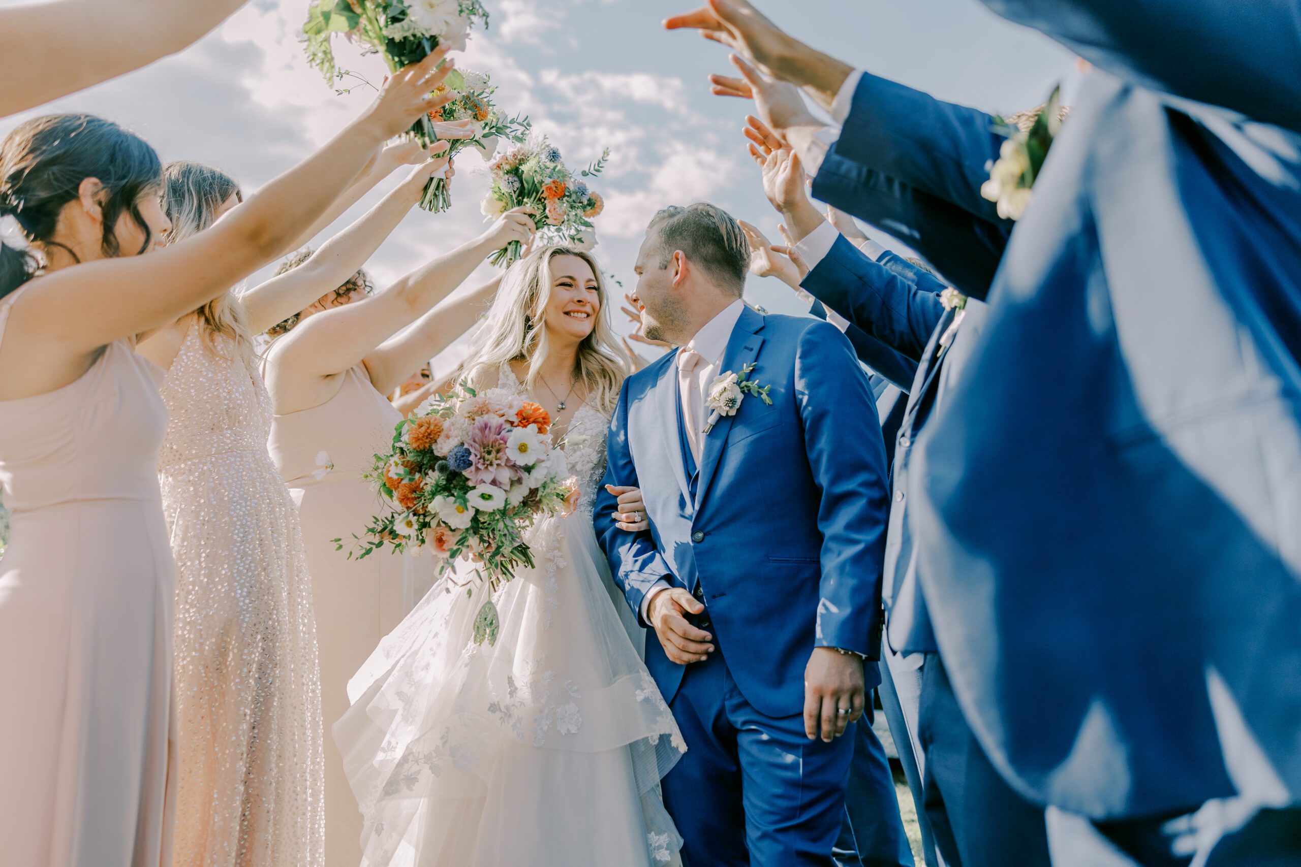 Bride and groom smiling at one another as they walk through a path of bridesmaids and groomsmen's hands overhead