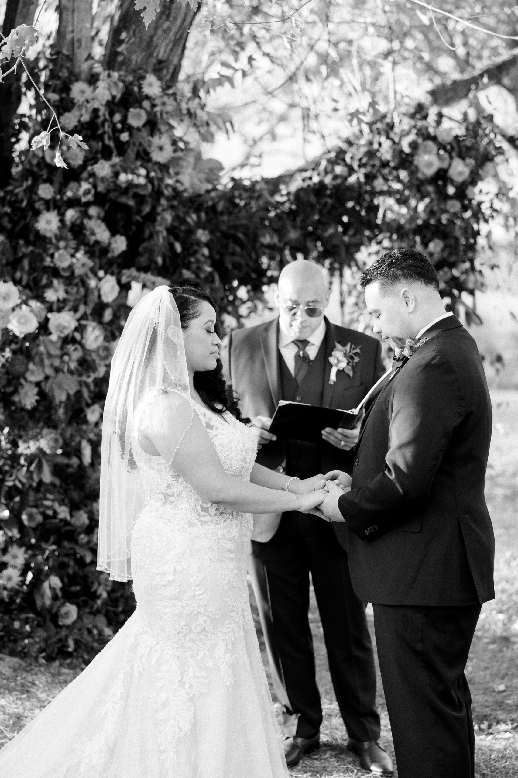 Black and white image of bride and groom holding hands with their eyes closed