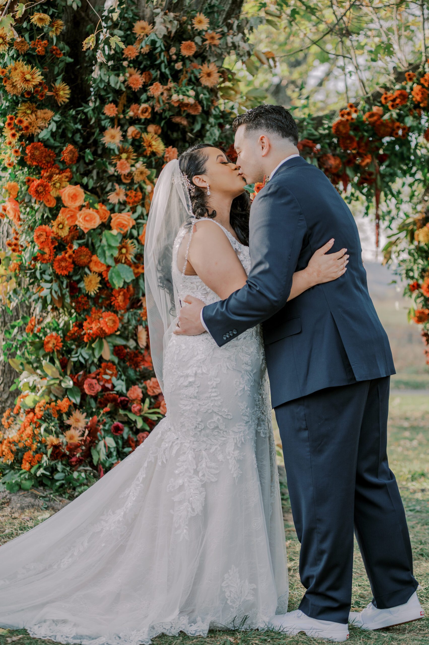 Bride and groom share their first kiss as husband and wife, orange and burgundy flowers behind them