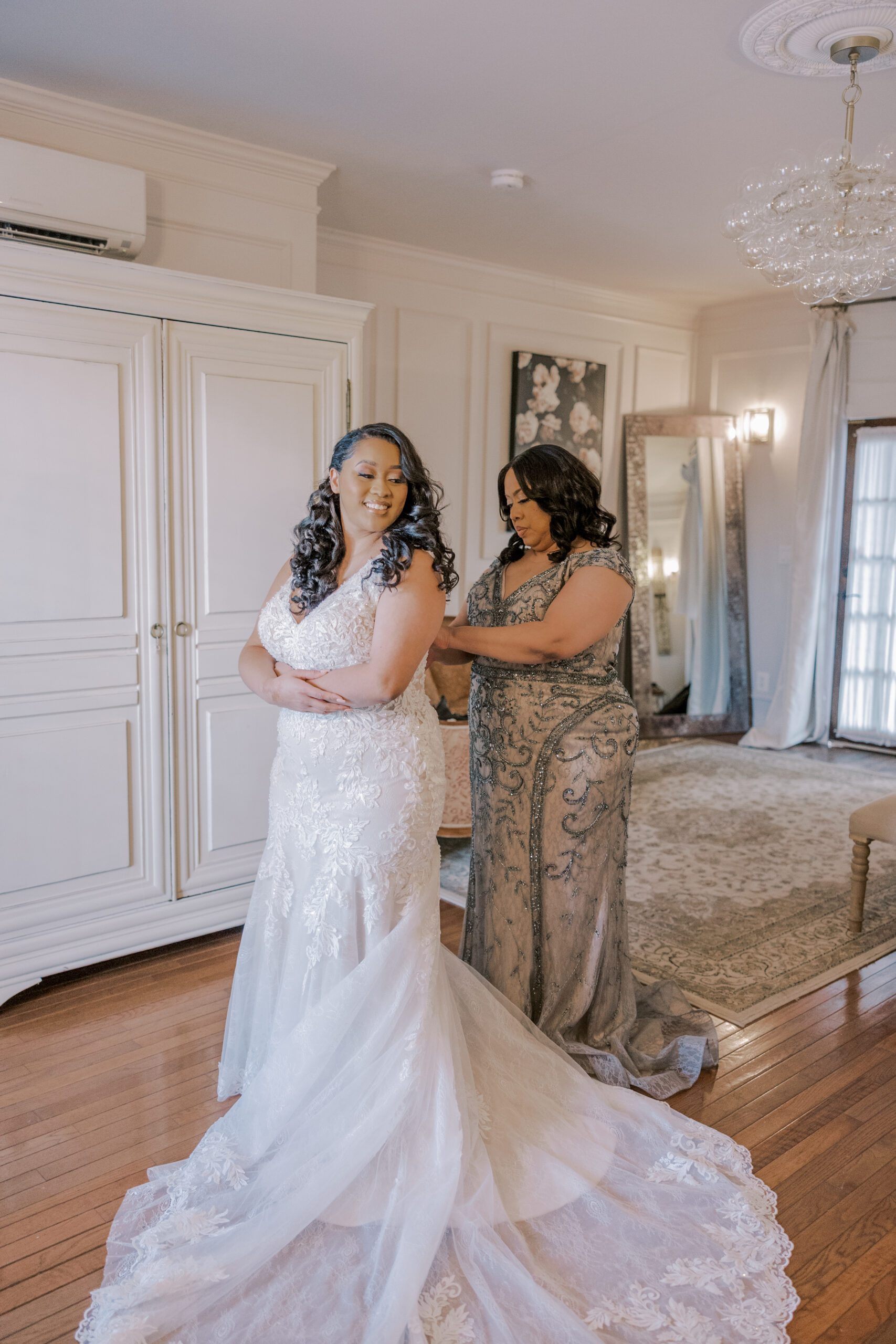 Full length photo of bride in her wedding dress while her mother adjusts the back of it