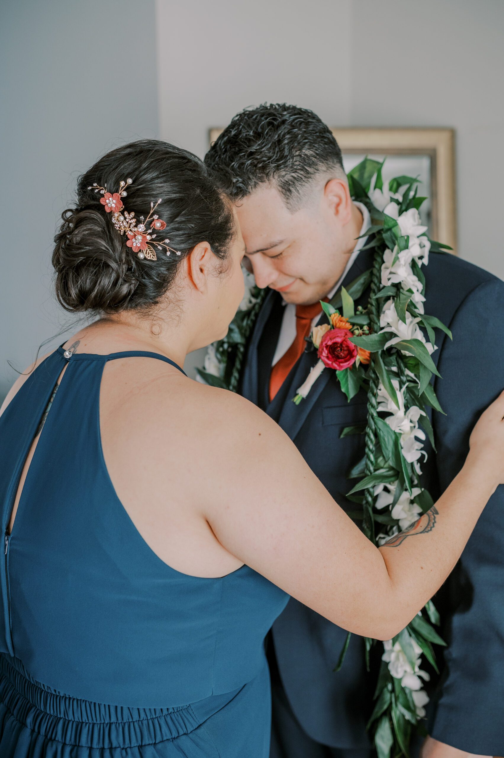 Groom wearing a floral lei while touching foreheads with a family member at the manor at airmont