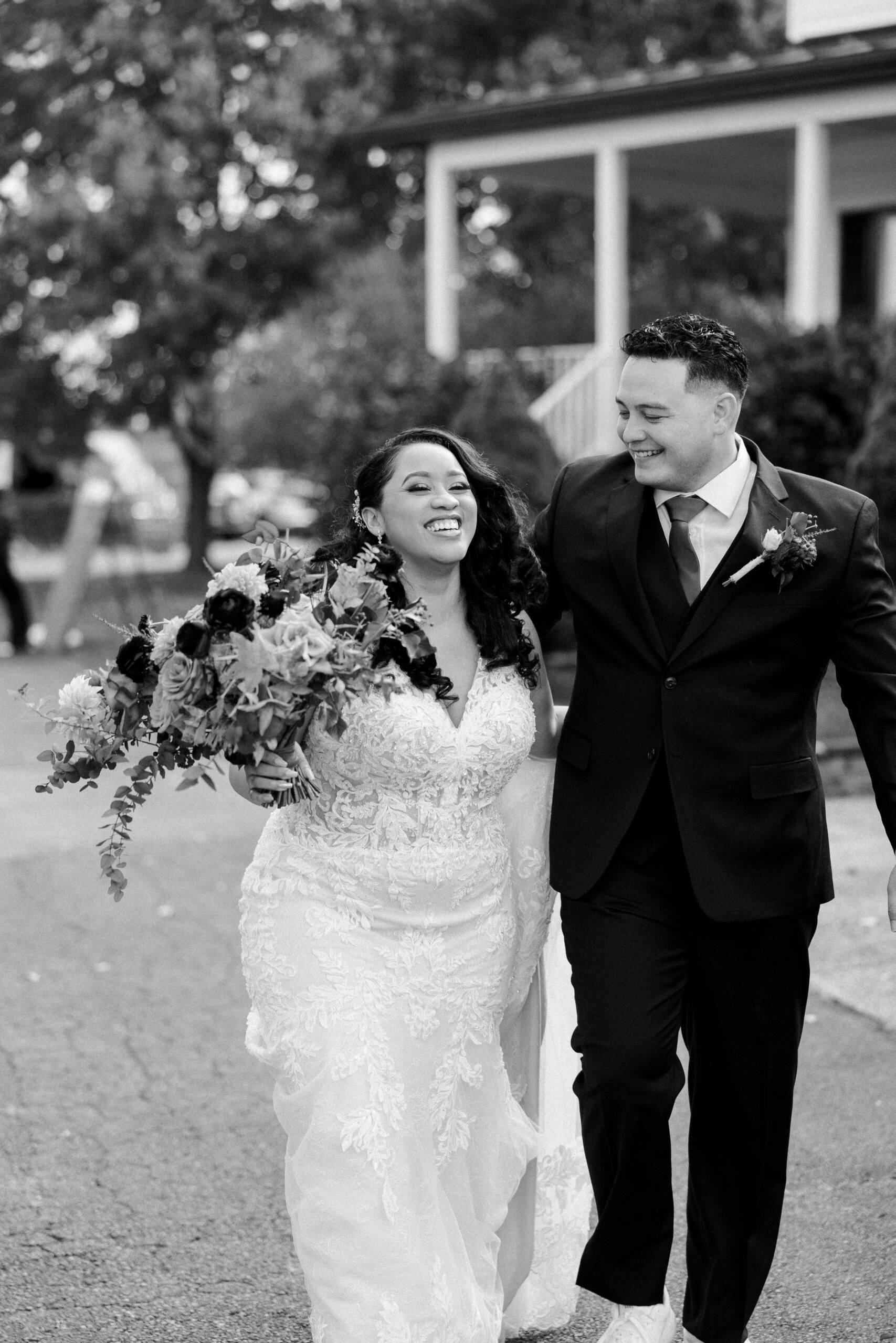 Black and white photo of bride and groom outside walking together and laughing as bride holds her bouquet