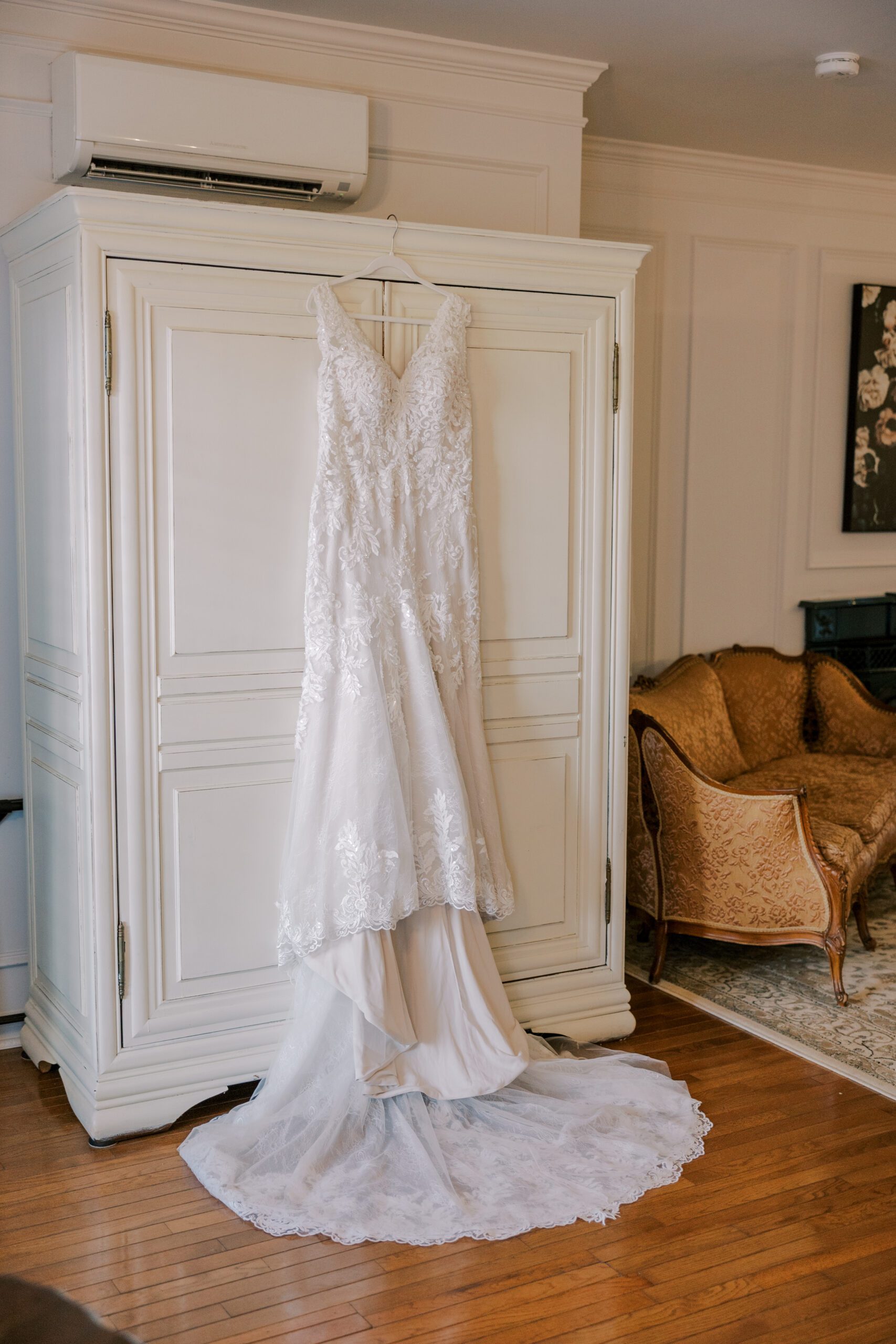Wedding gown hanging on a white armoire, wooden floors and a gold colored couch in background
