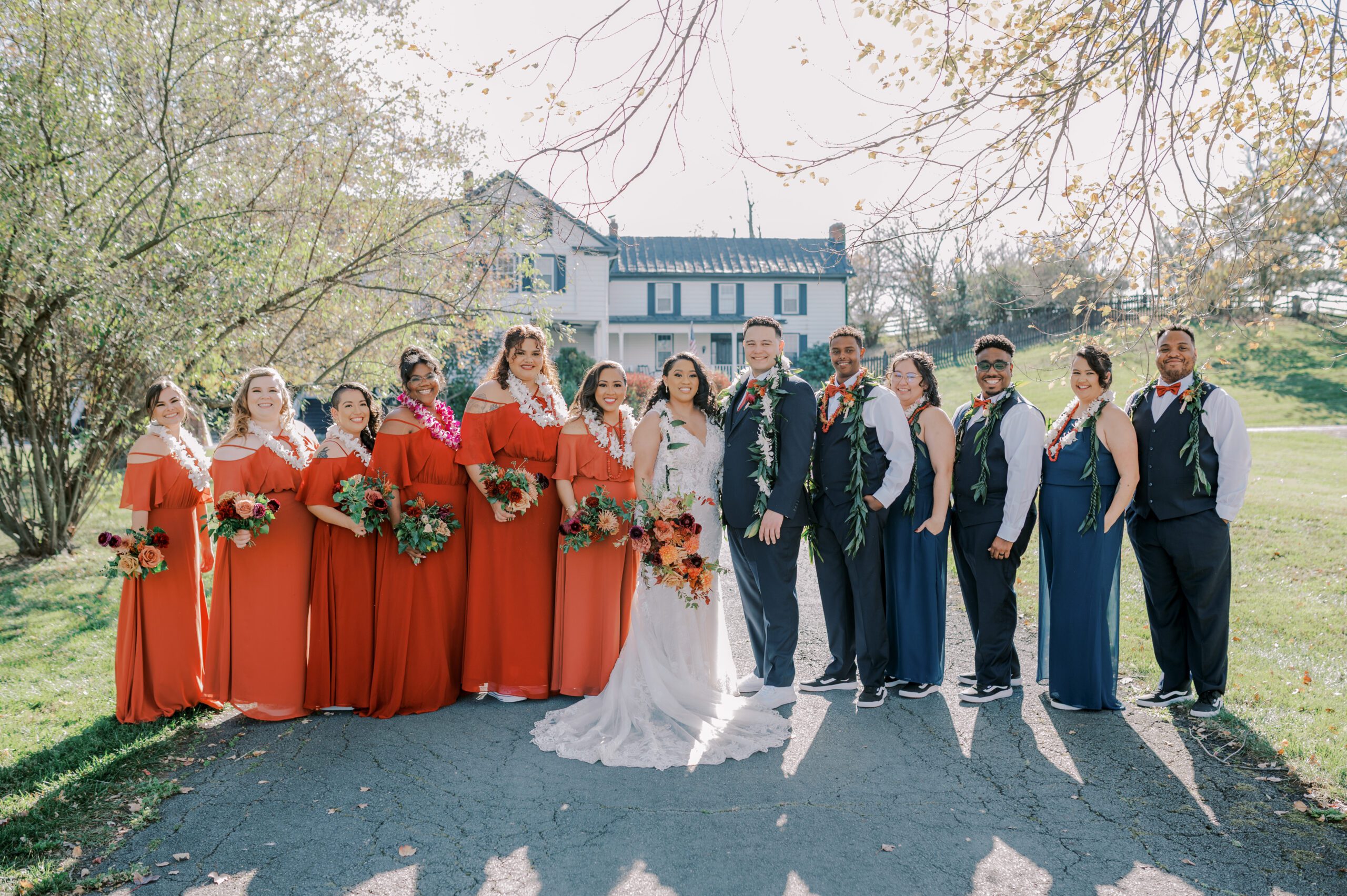 Outdoor group photo of couple with wedding party, all smiling and facing the camerg while wearing leis