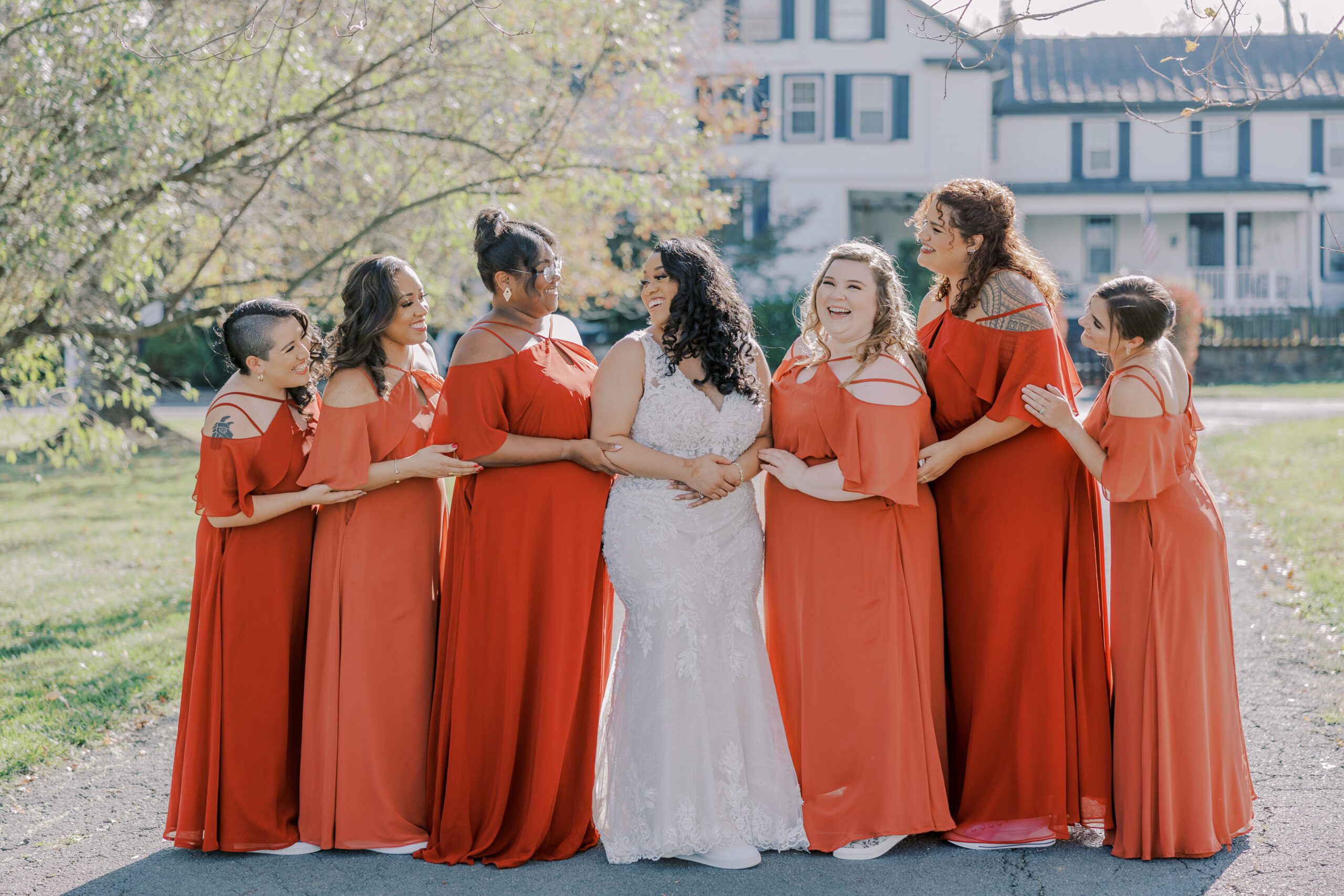 Bride and her bridesmaids arm in arm, smiling and laughing at each other