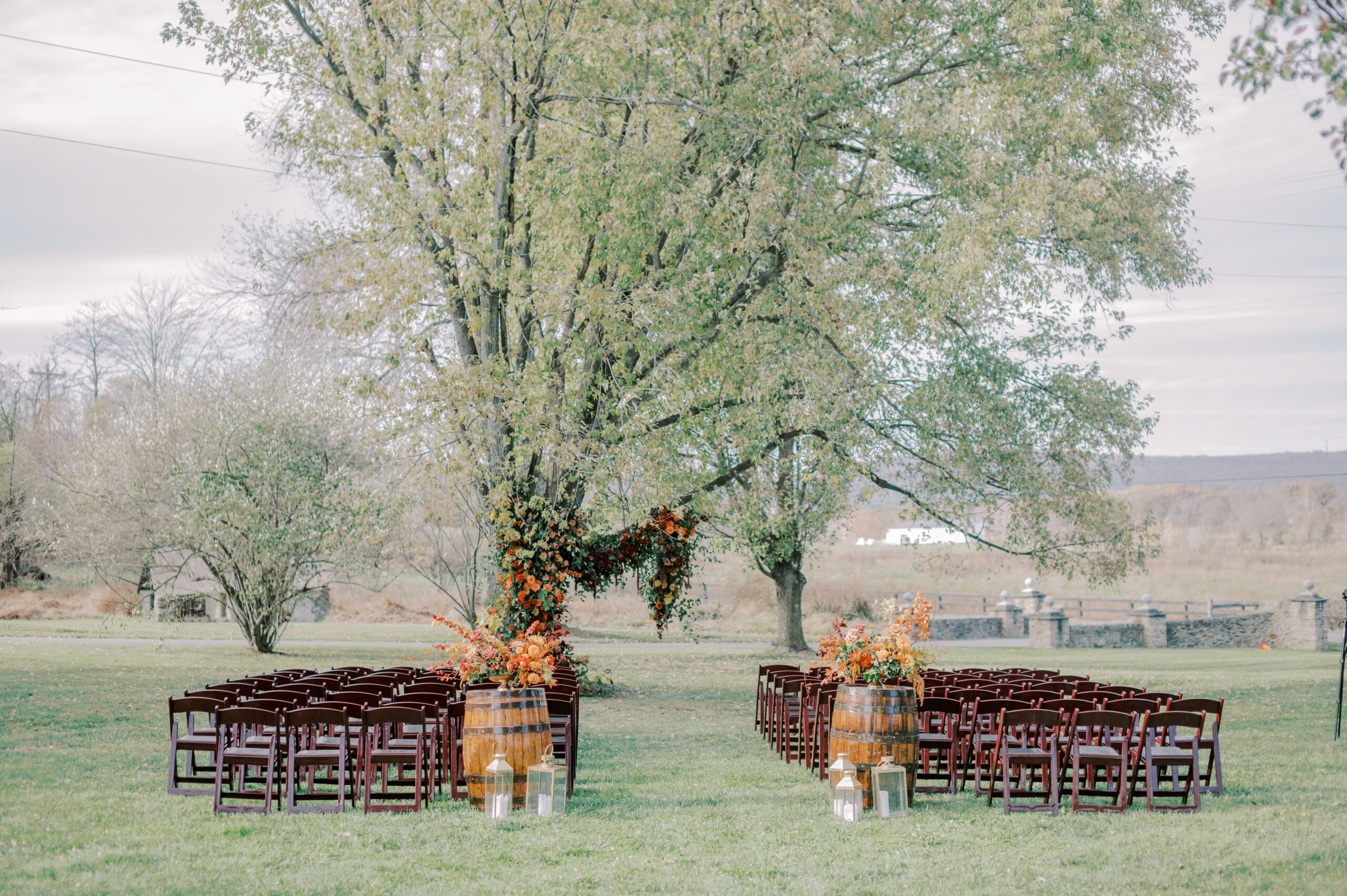 Photo of ceremony spot at the manor at airmont, dark wooden chair, a tree with hanging florals, and barrels with more floral arrangements