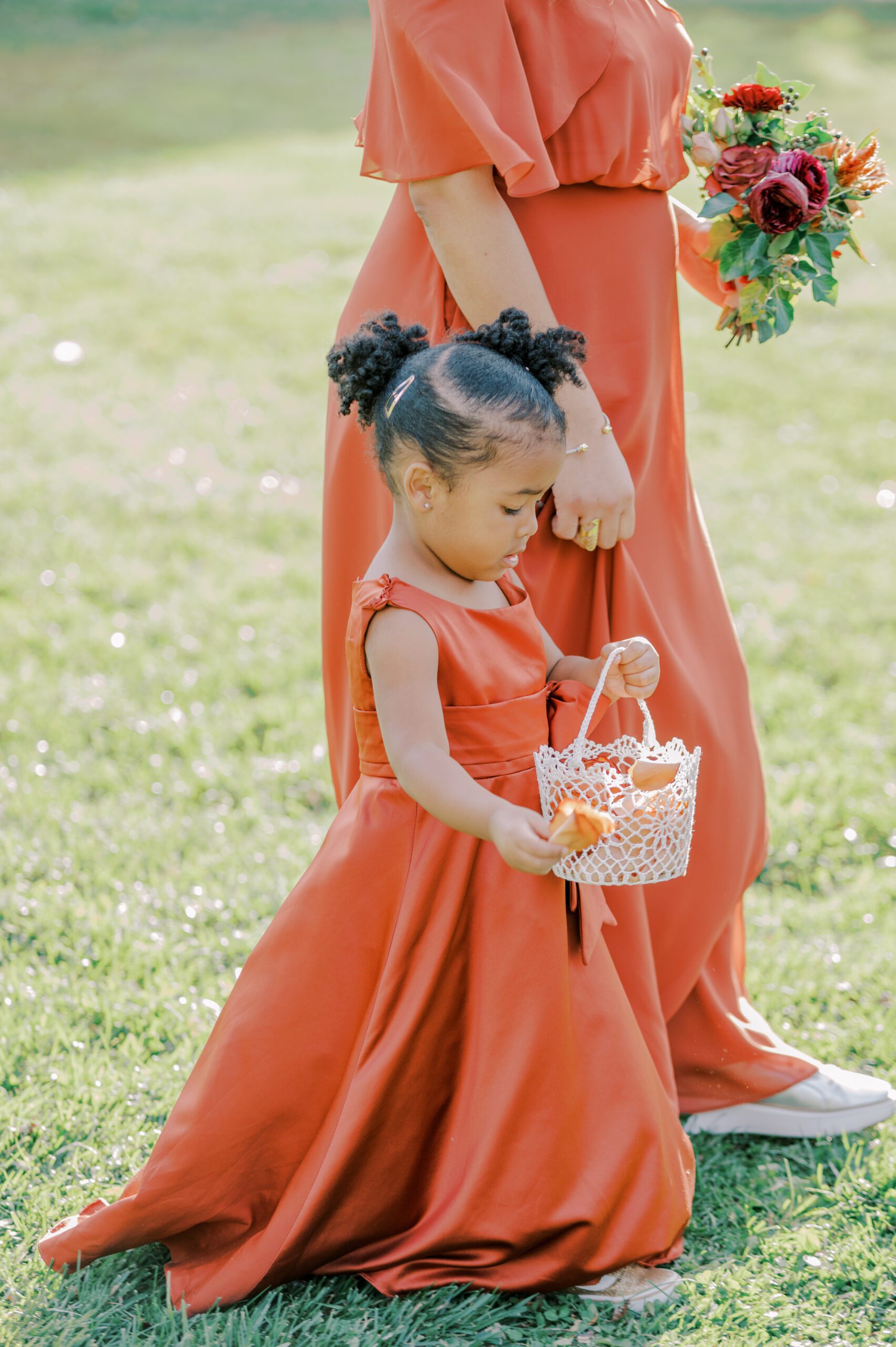 Image of young girl in orange dress tossing flower petals as she walks down the aisle alongside a bridesmaid in an orange dress
