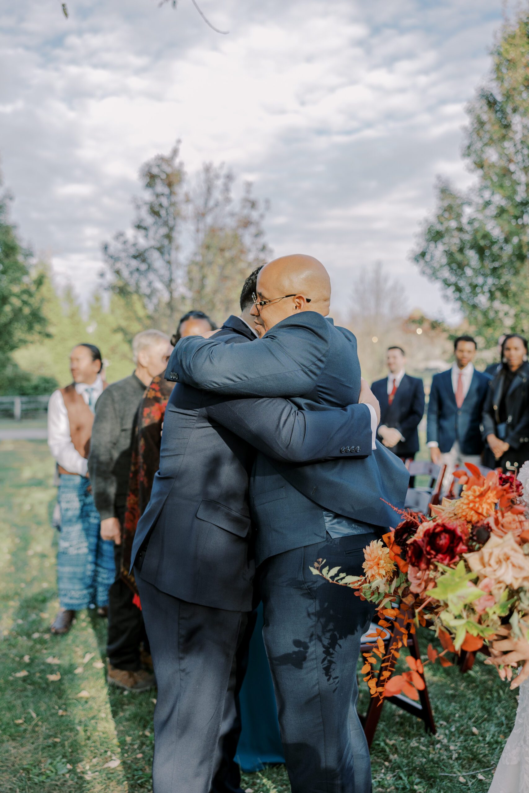 Groom and bride's father share a hug at the alter, guests standing in background at the manor at airmont fall wedding