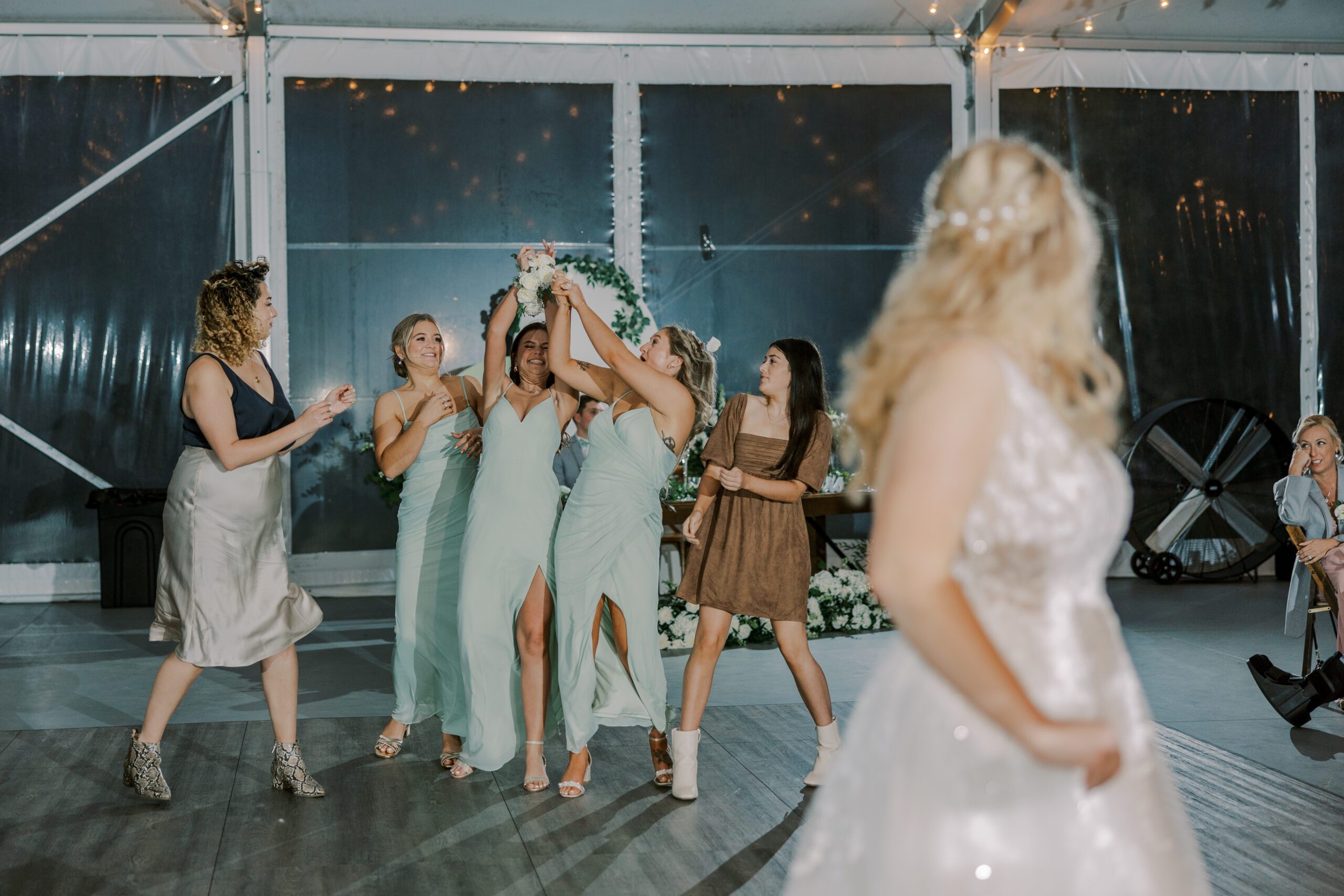 Bridesmaid catching the bouquet as a couple other guests and bridesmaids stand nearby