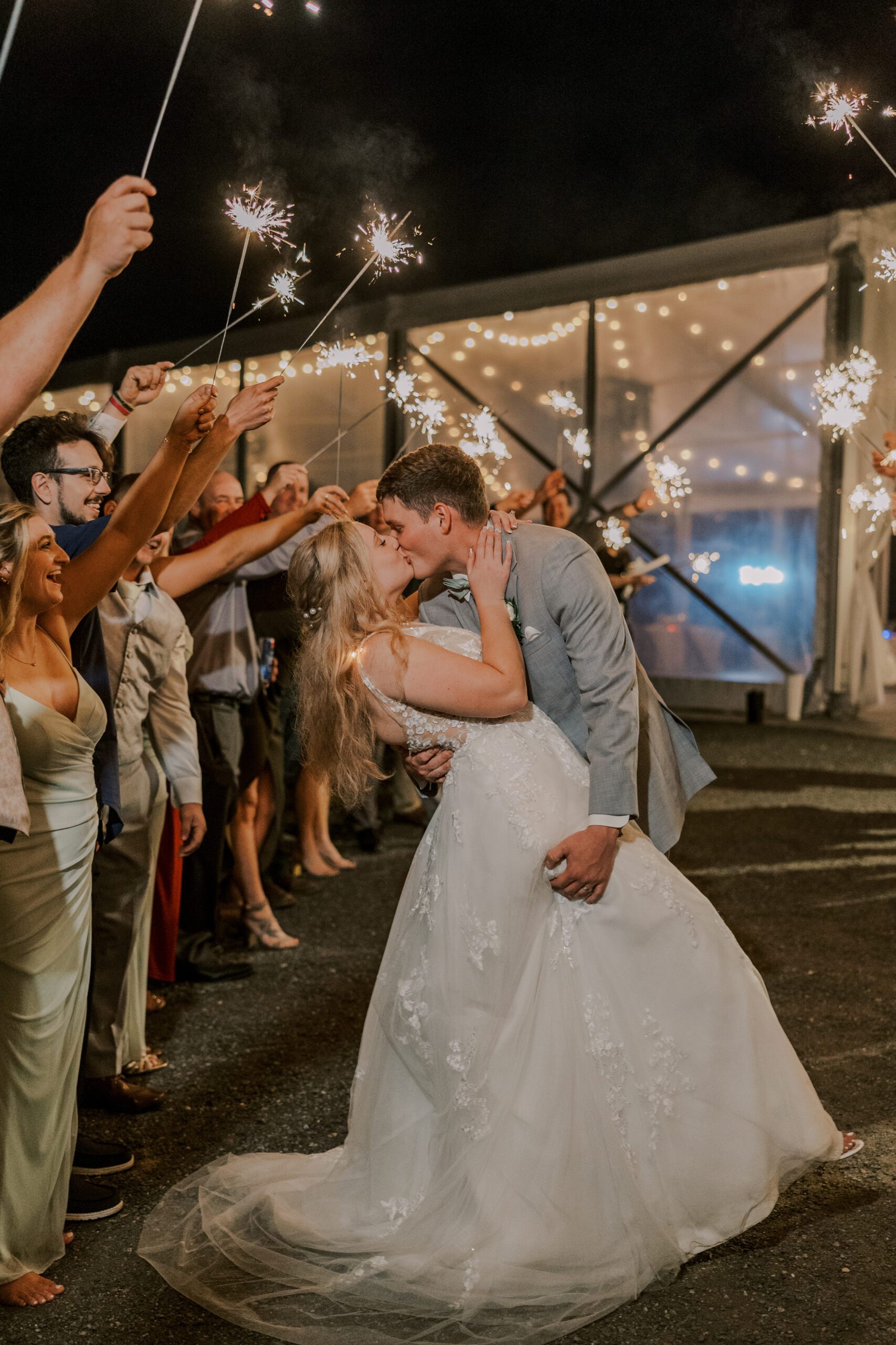 bride and groom sharing a kiss as they exit the reception, guests line either side of their path holding sparklers
