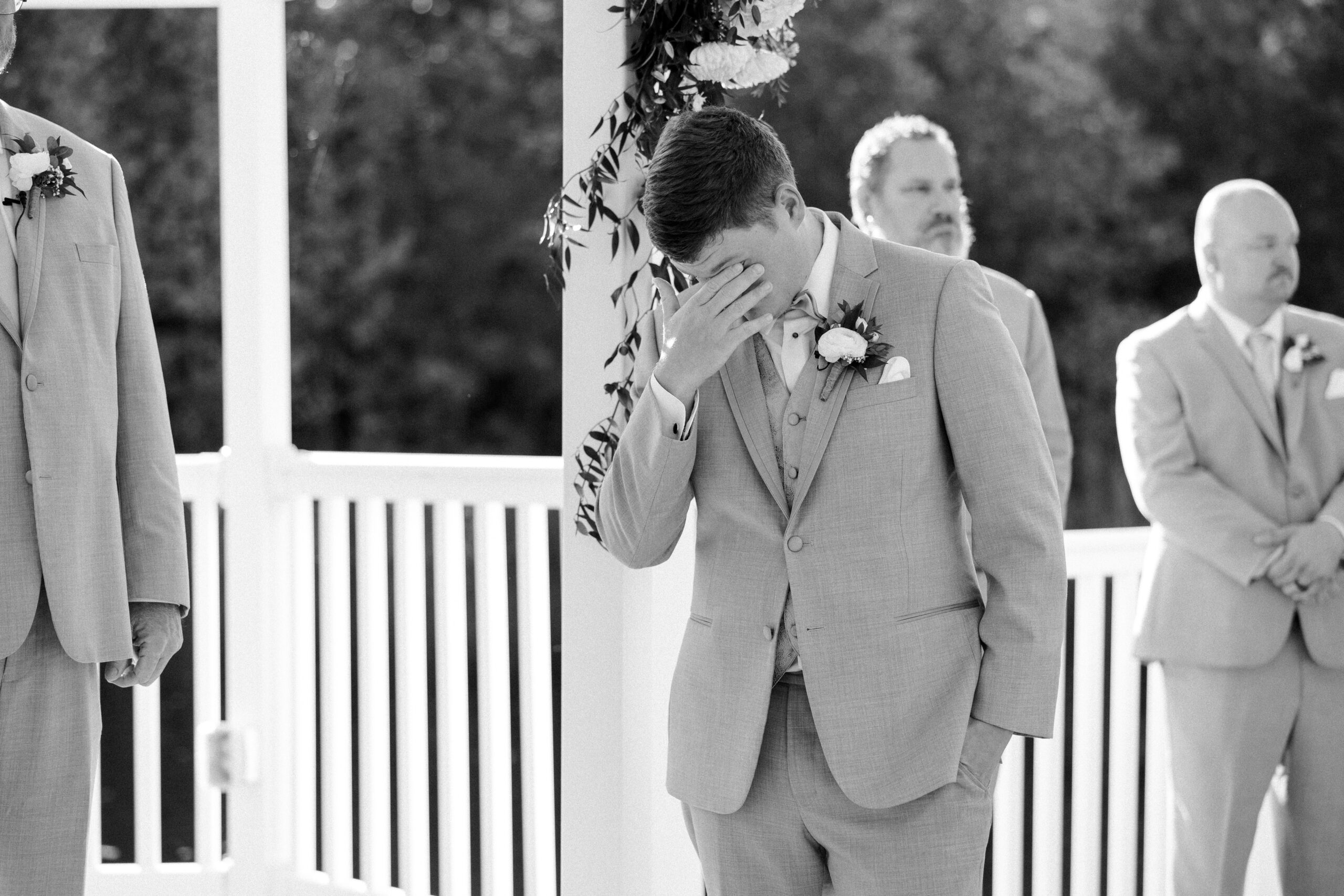 Black and white image of groom emotional with his hand covering his face as he wipes his eyes