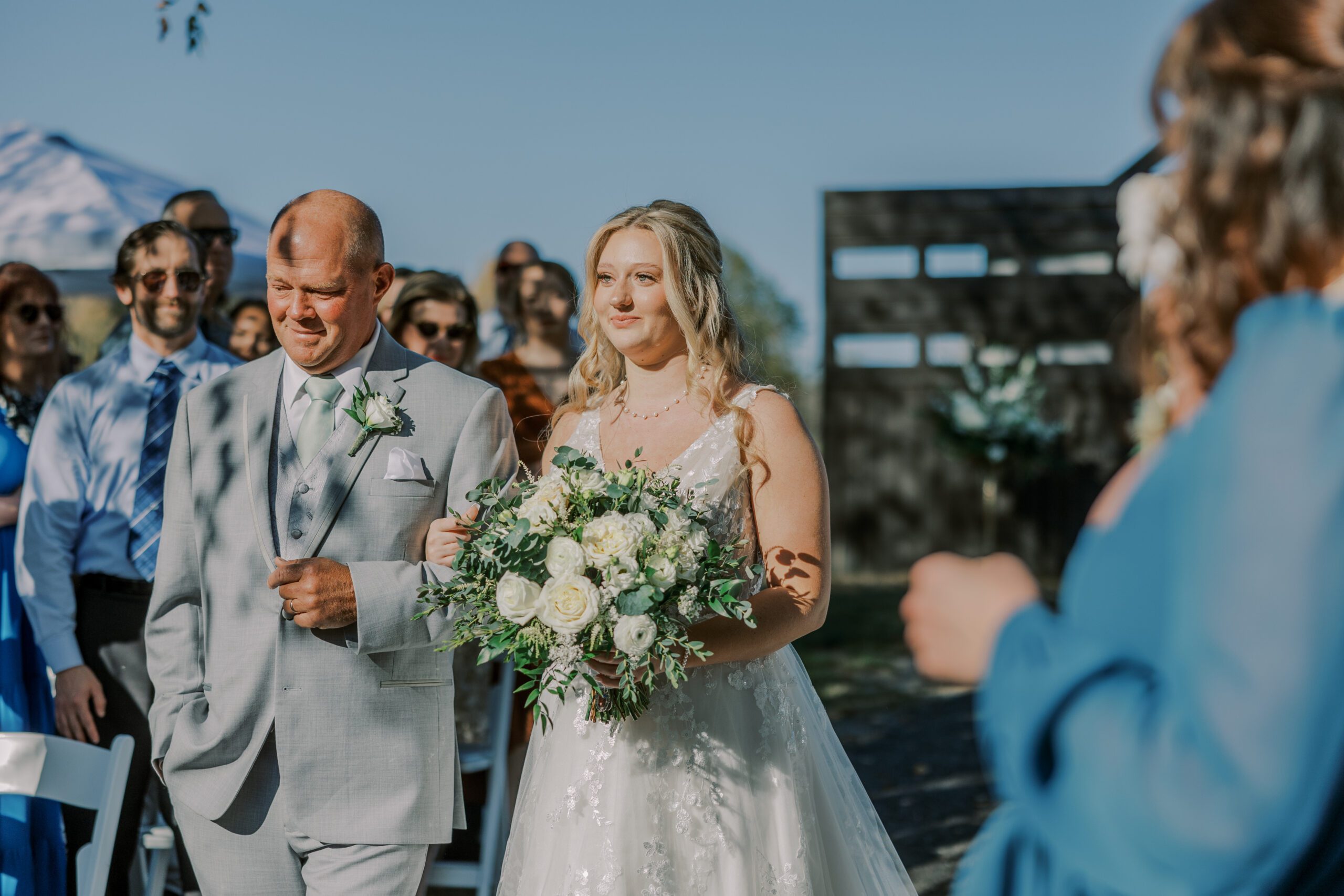 Bride and her father walking down aisle, bride is holding a large bouquet of white flowers and greenery