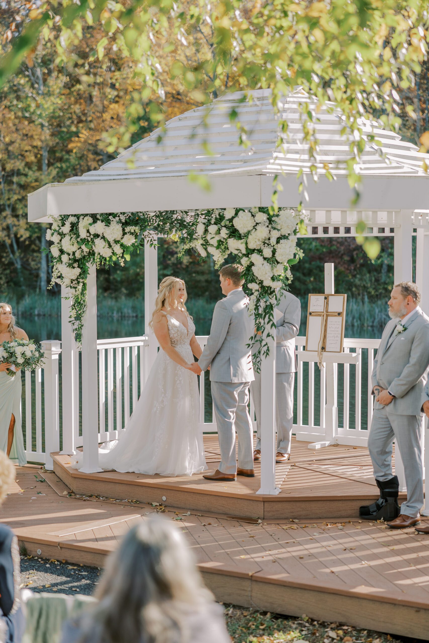 Bride and groom stand holding hands under the white gazebo at their arbor haven fall wedding