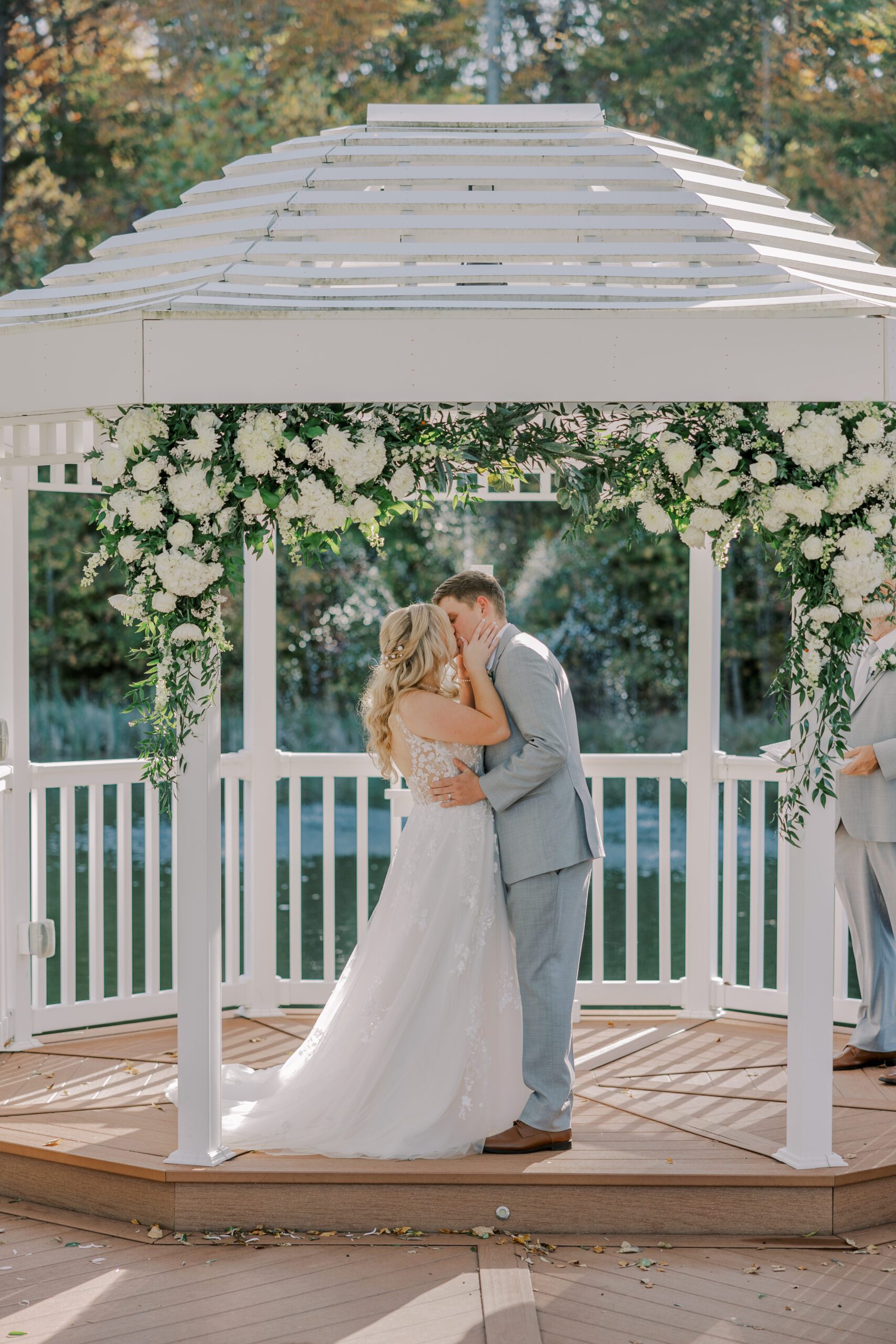 Bride and groom kissing under the white gazebo, groom's hands on are on bride's waist and bride's hands are on grooms face