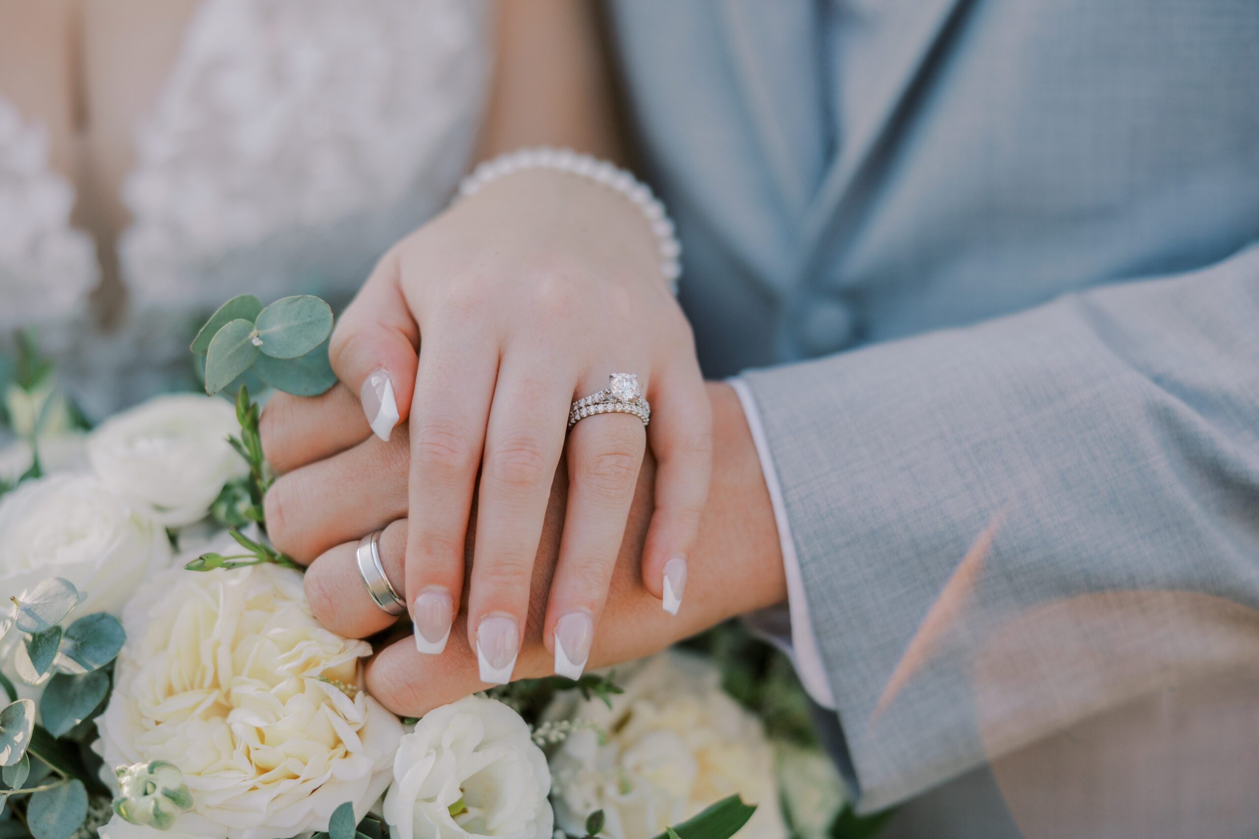 Close up image of bride and groom's hands showing off their wedding rings with bride's bouquet in background