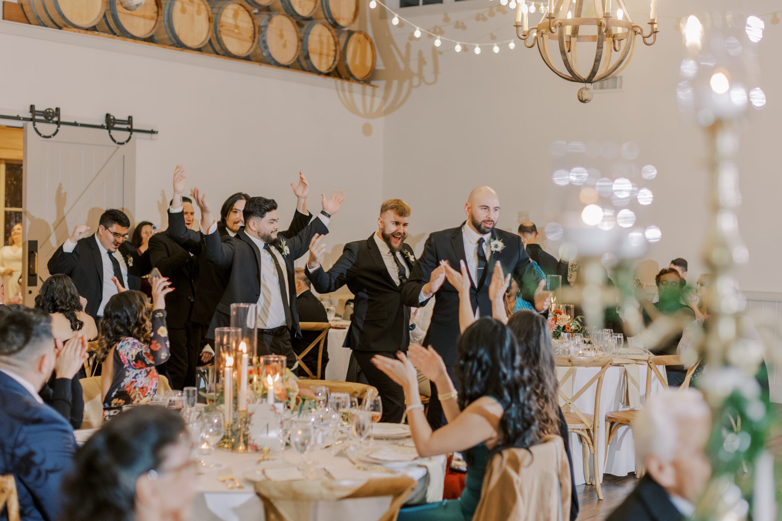 Groomsmen enter the reception with hands in air, cheering and smiling