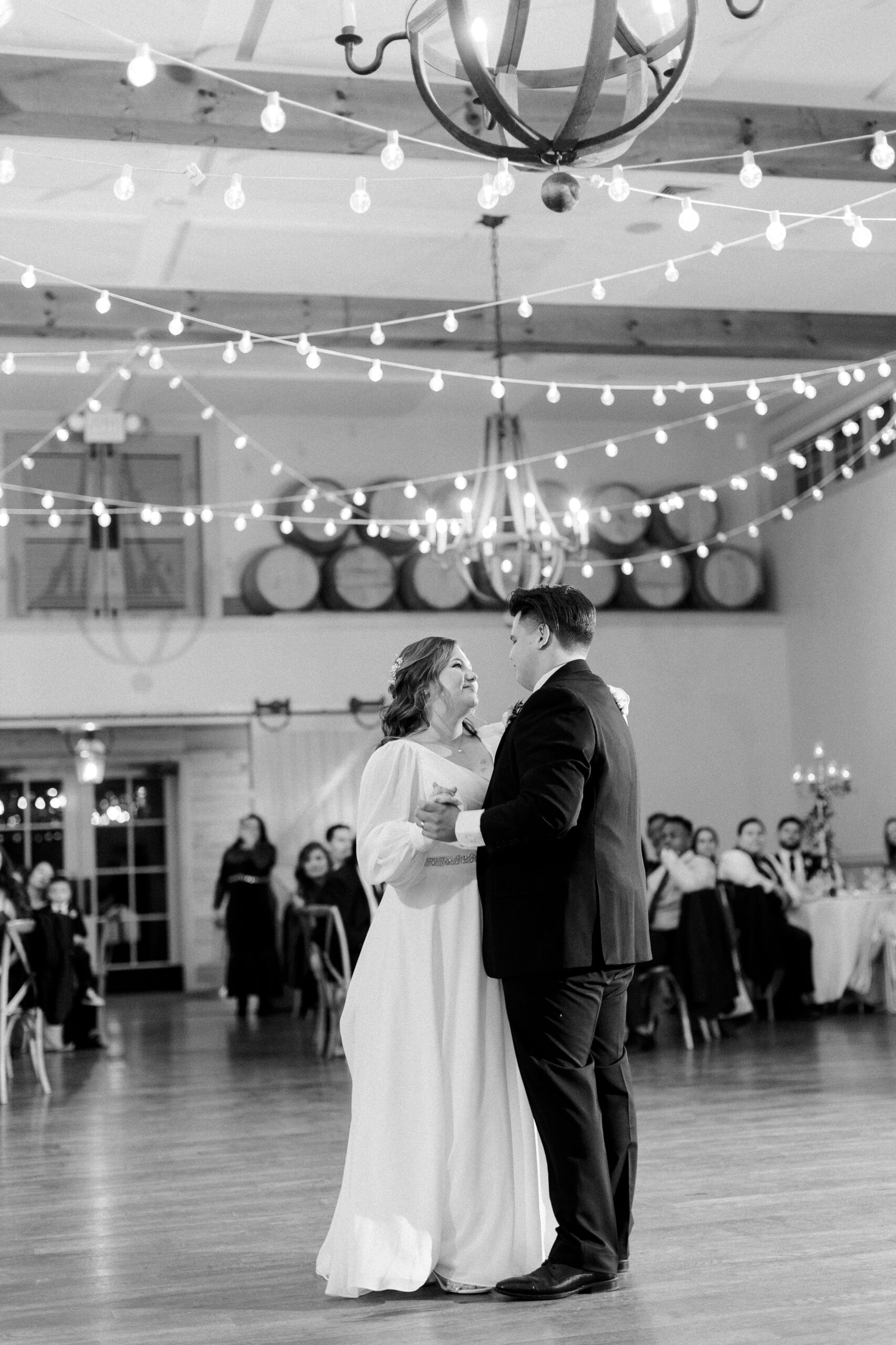 Black and white photo of bride and groom dancing under string lighting at king family vineyards