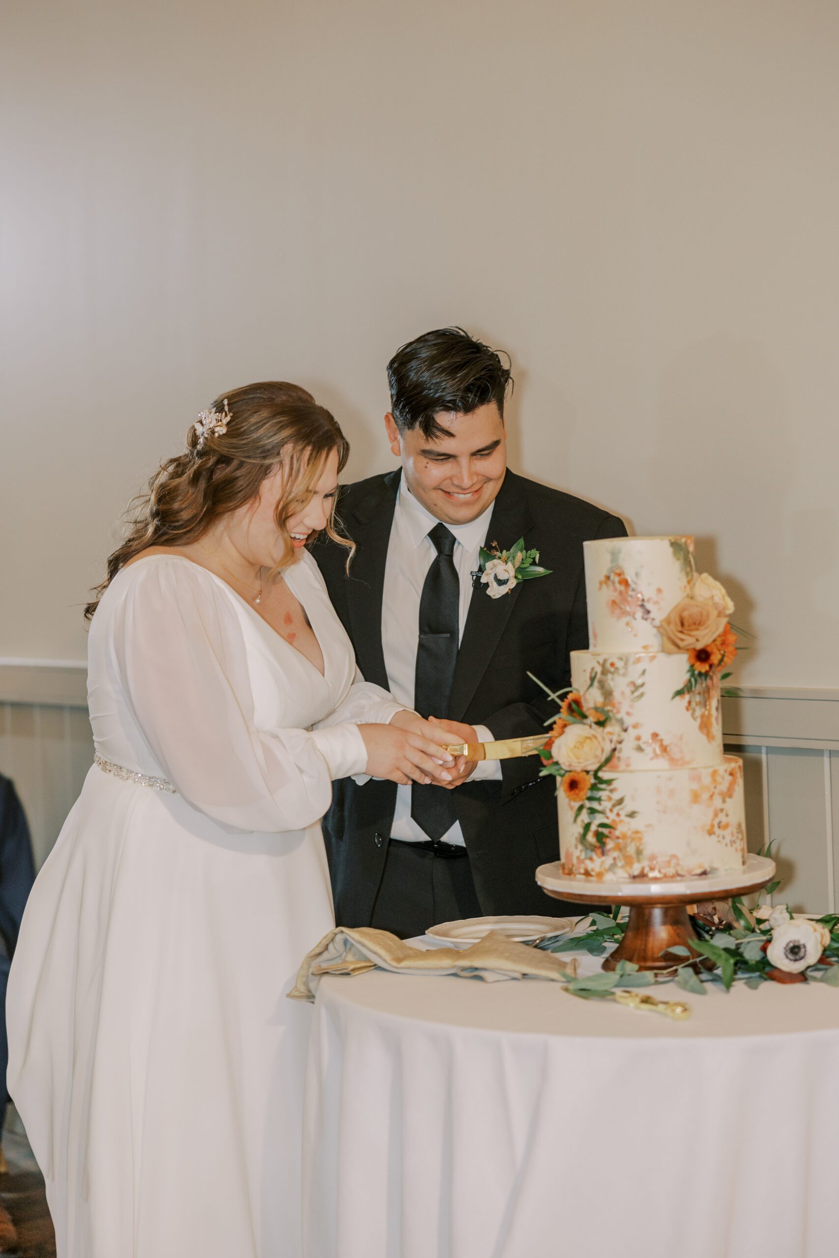 Bride and groom cutting their wedding cake that has orange and off white flowers on it