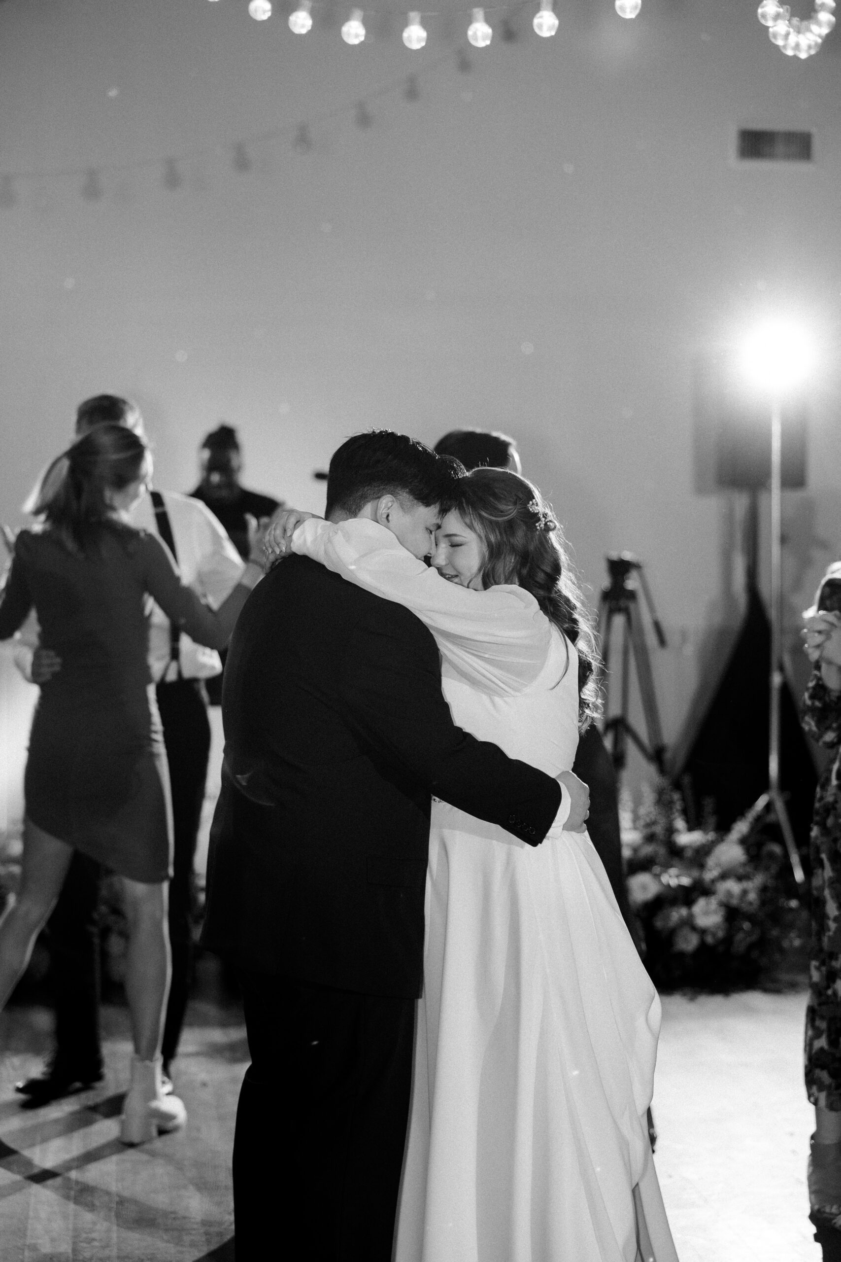 Black and white photo of bride and groom on dance floor while other guests dance in background