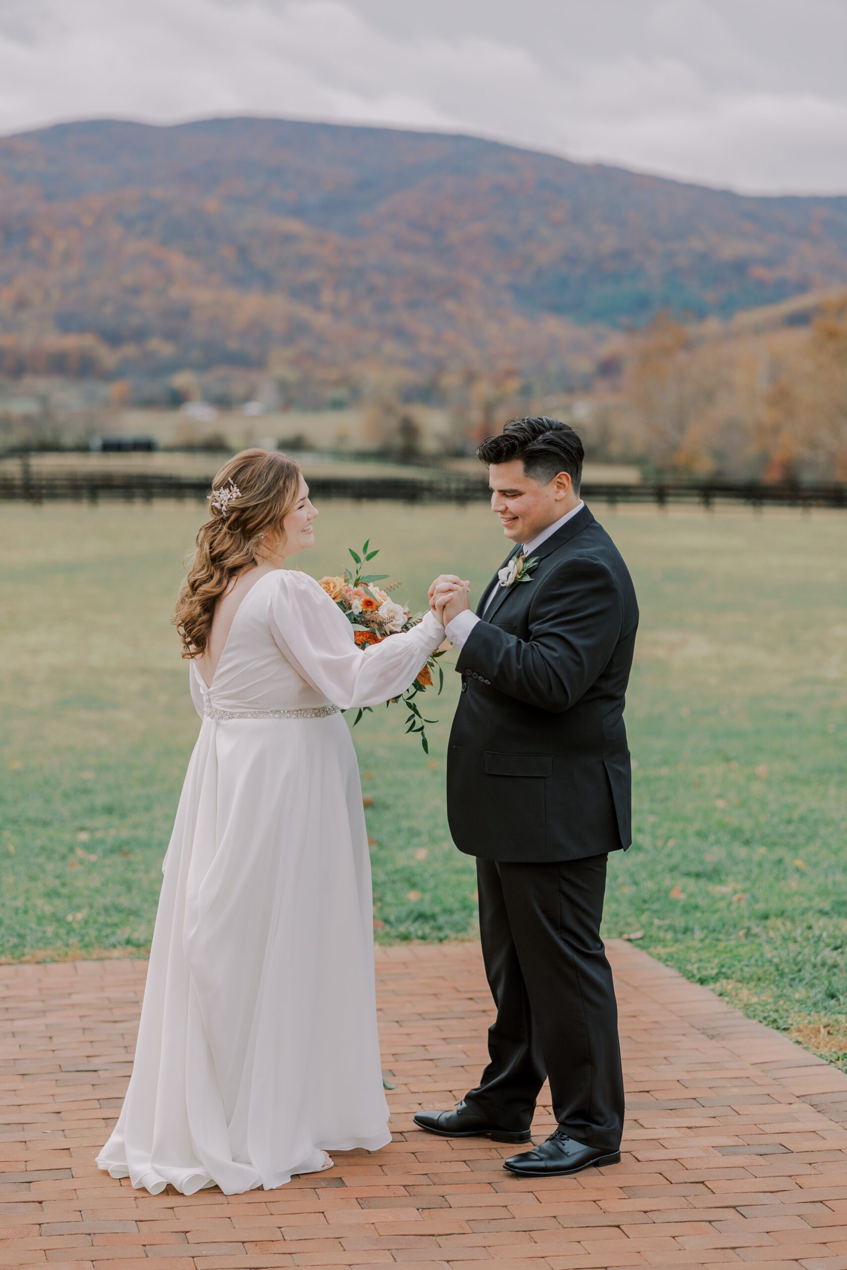 Groom and bride hold hands with beautiful mountains in background covered in orange trees