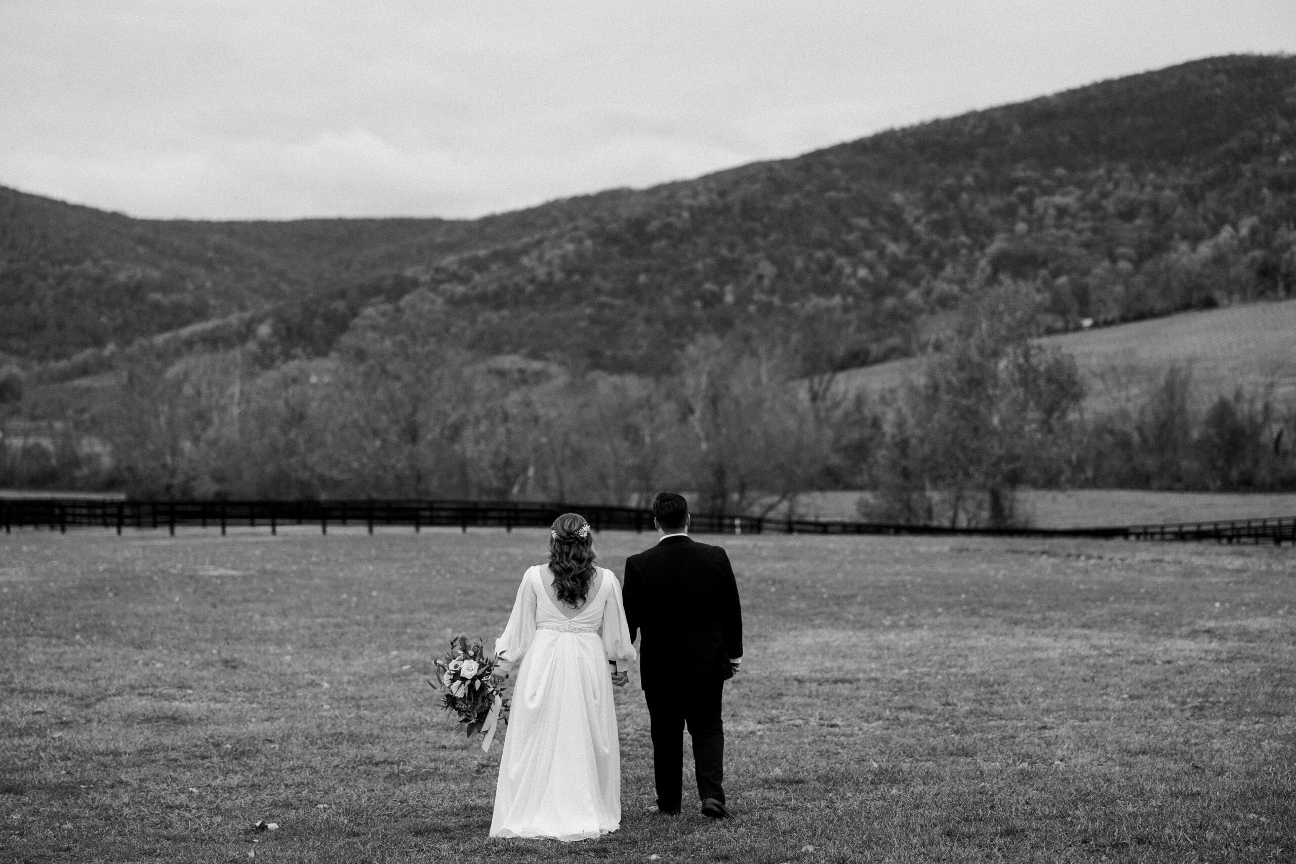 Black and white image of bride and groom walking away from camera towards the mountains