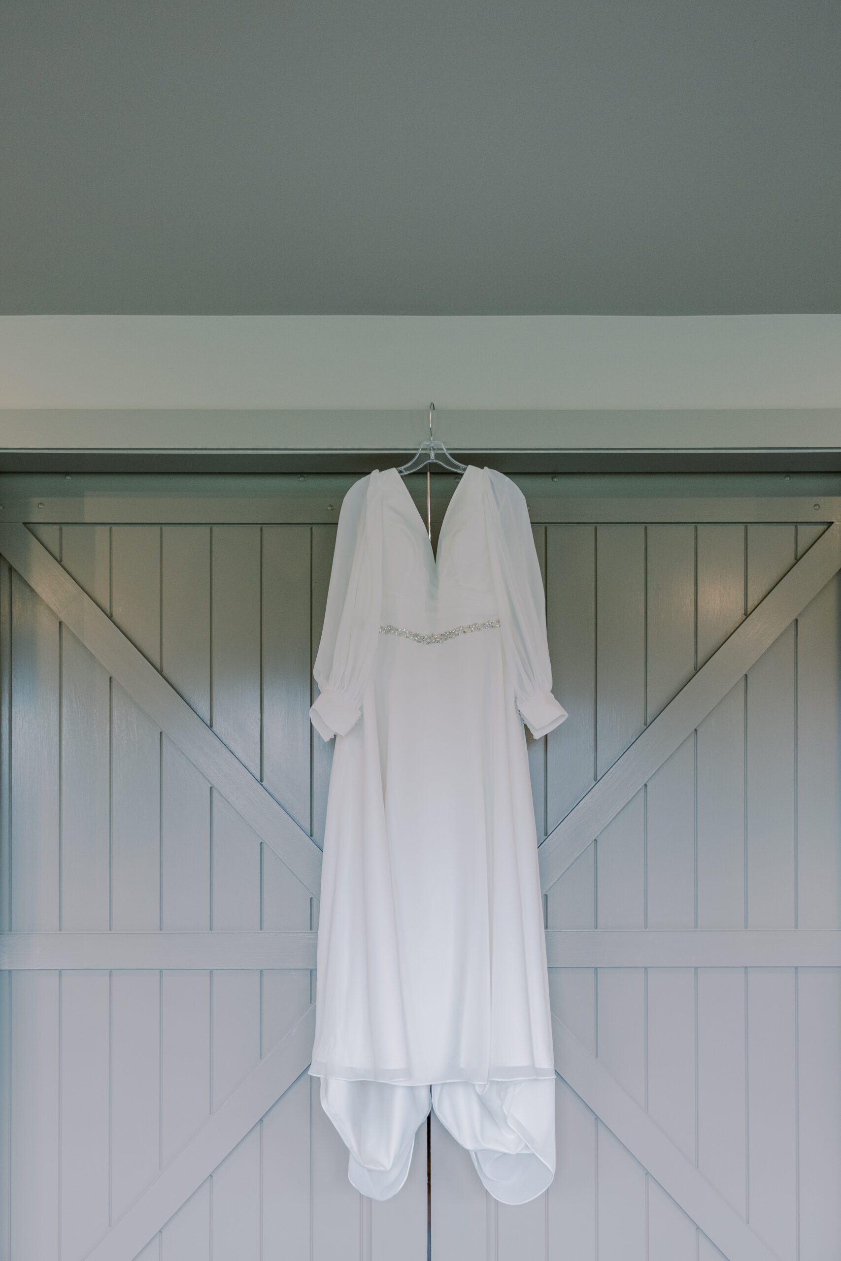 White long sleeve wedding dress hanging in front of light grey wood slat doors at king family vineyards