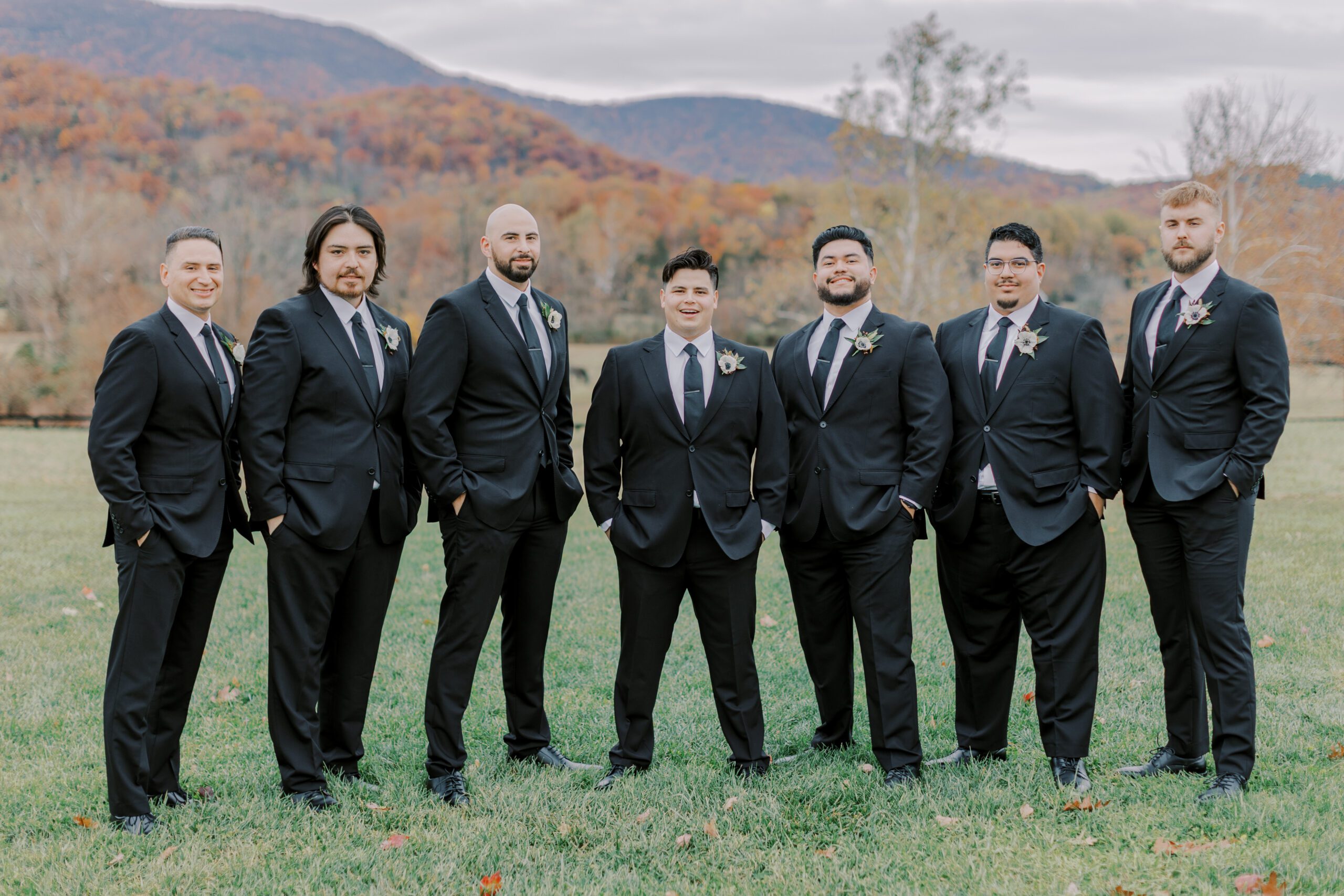 Image of groom and his groomsmen standing outside with fall colored scenery in background