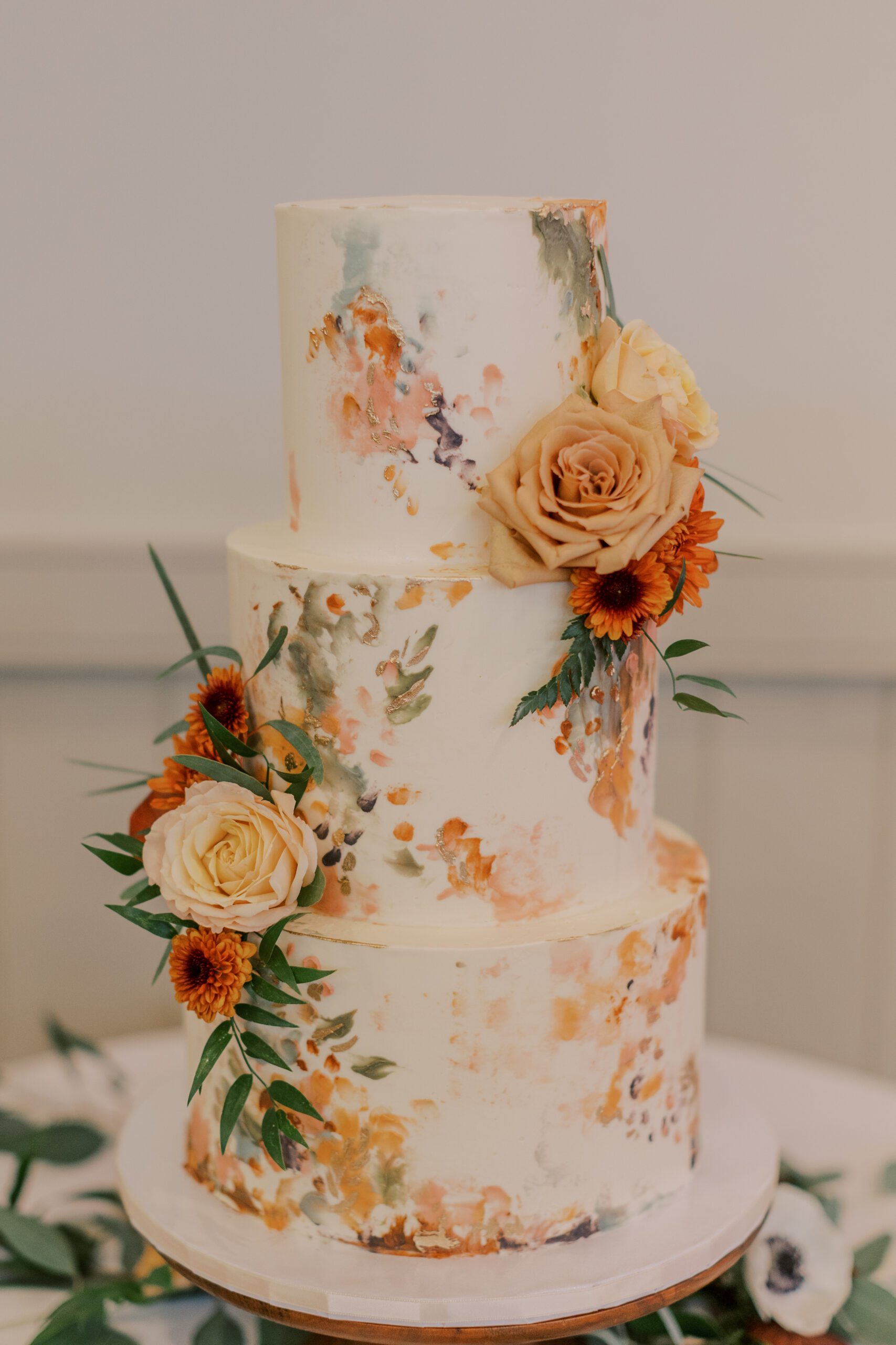 Image of three tiered off white wedding cake with orange, and green tones and flowers added to it