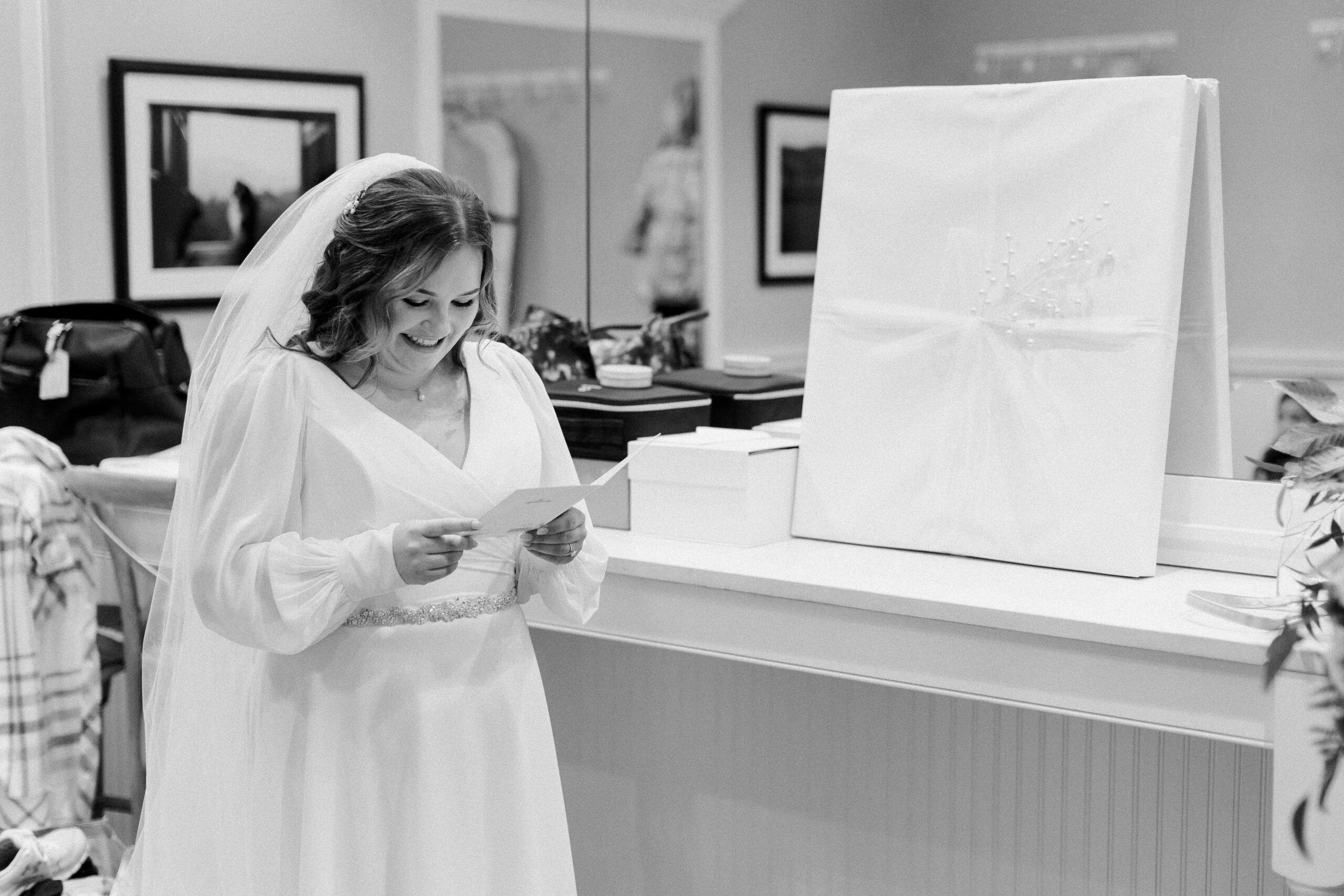 Black and white image of bride smiling reading a card standing next to a wrapped gift