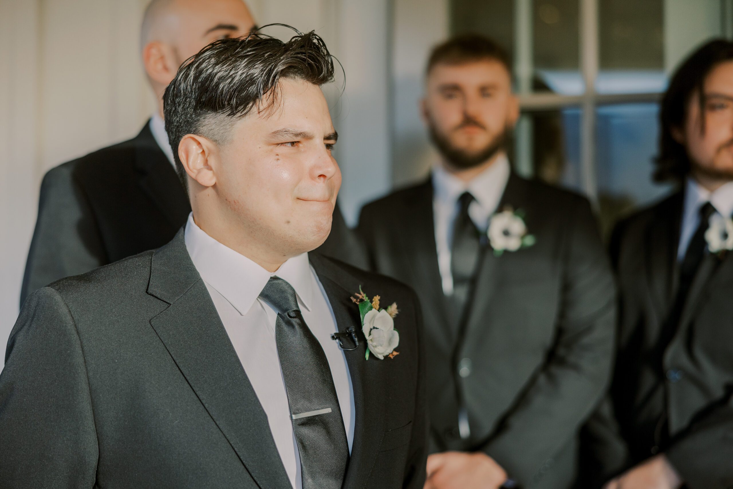 Emotional photo of groom looking up the aisle, his groomsmen pictured in the background