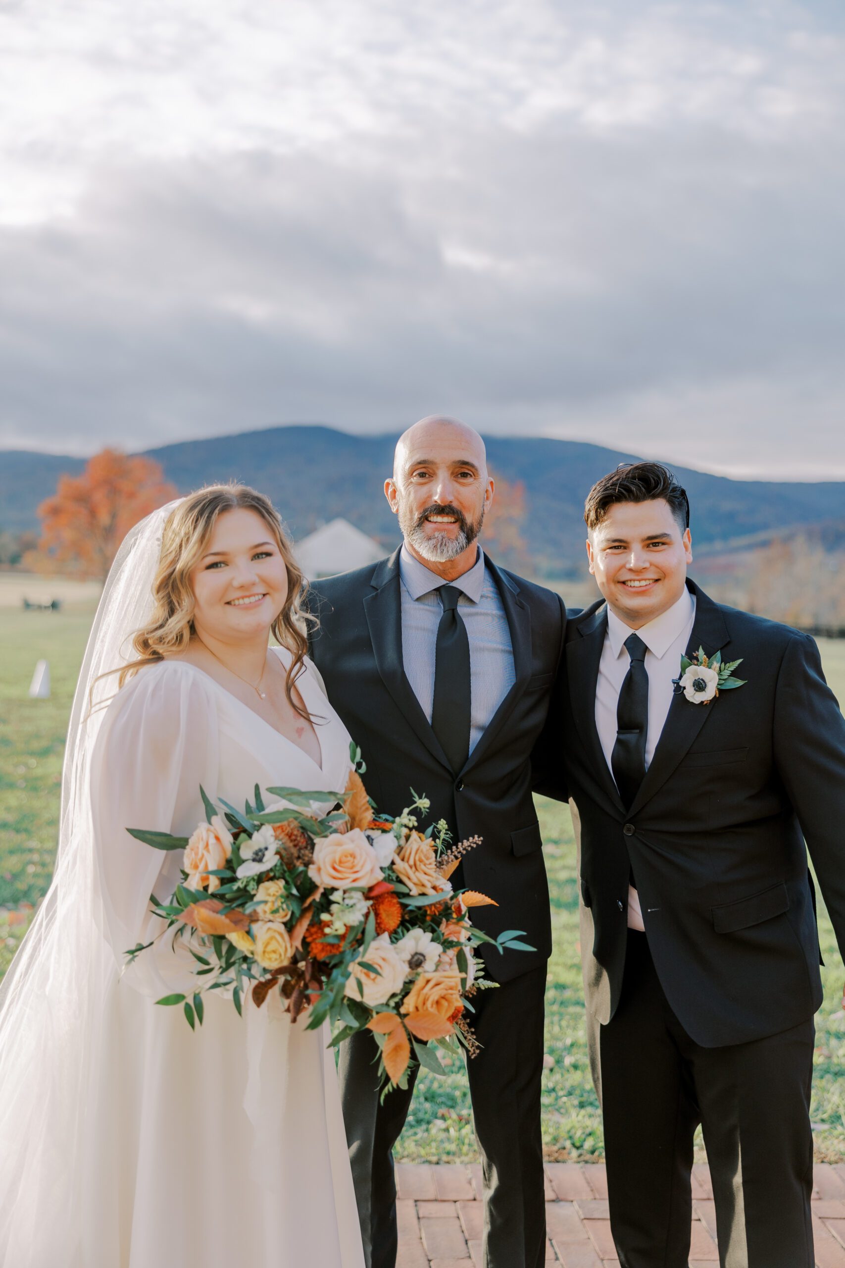 Photo of bride and groom with their officiant, mountain scenery in background