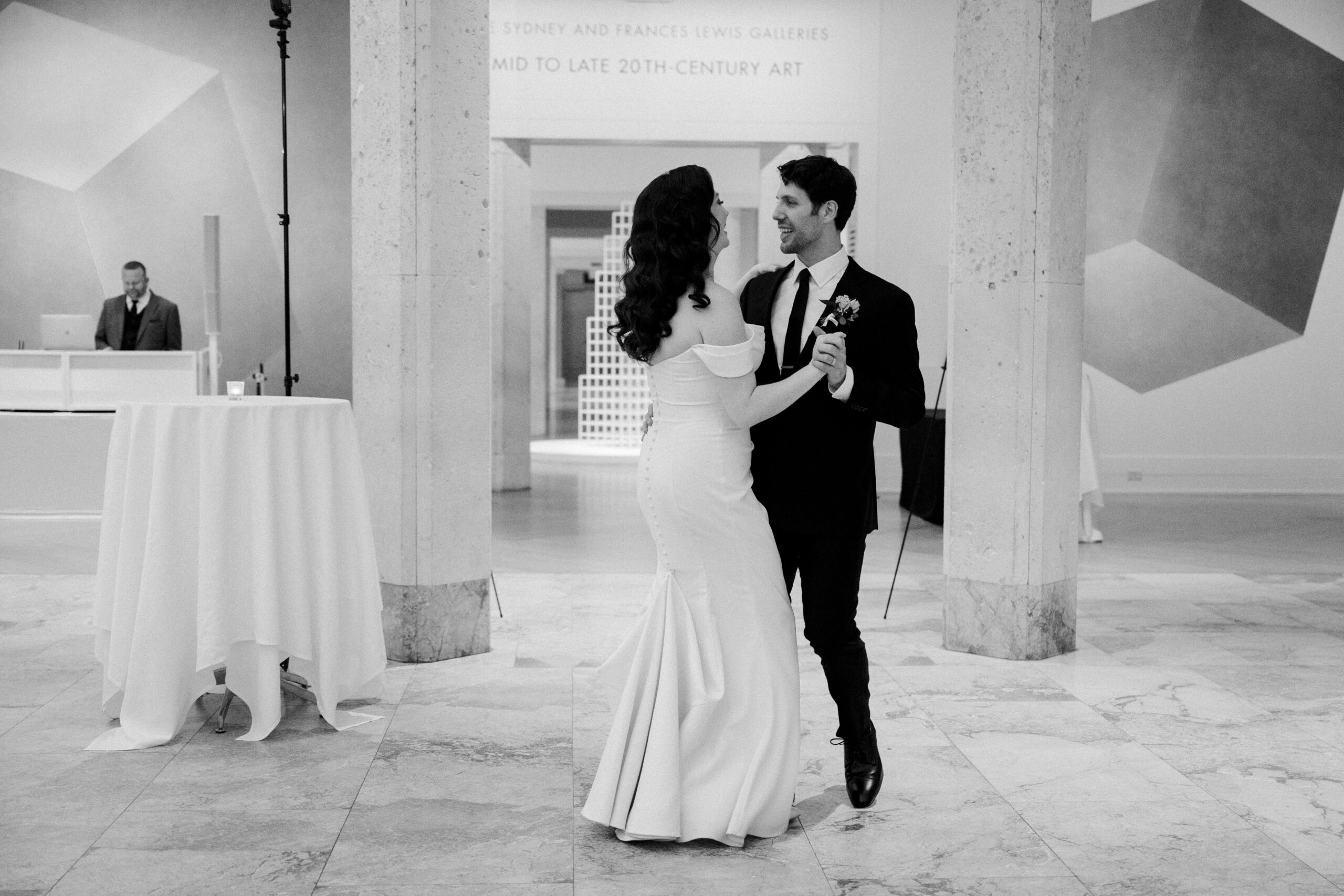 Black and white photo of bride and froom slow dancing, big stone columns behind them