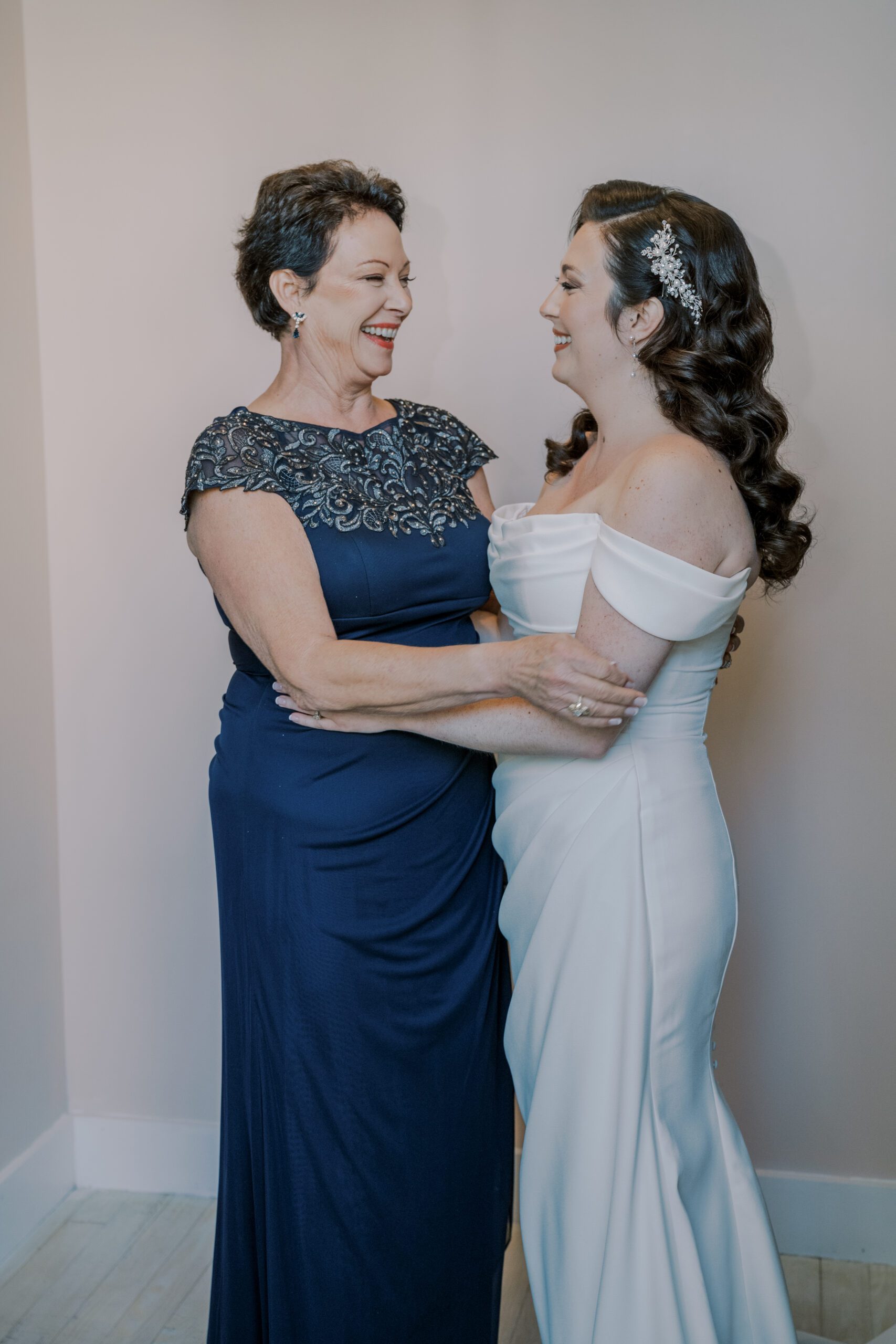 Bride and her mother who is wearing a blue dress with beading around the chest and shoulders, smiling at one another