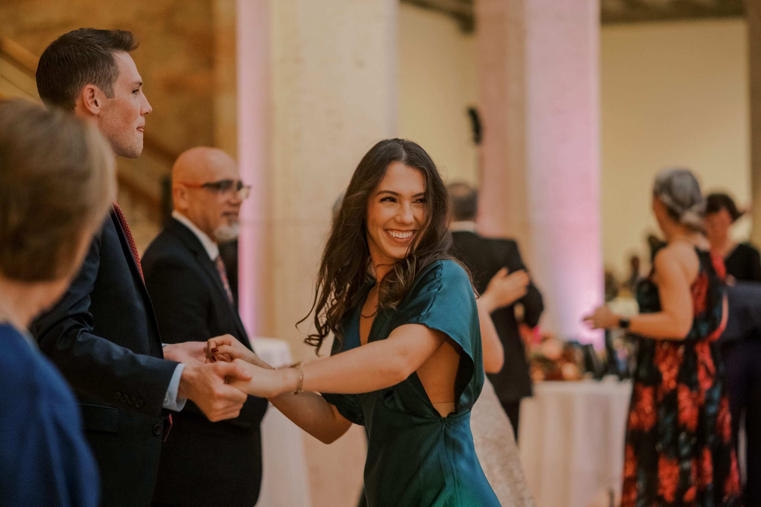 Brunette woman wearing a blue dress dancing, other guests can be seen in background dancing as well