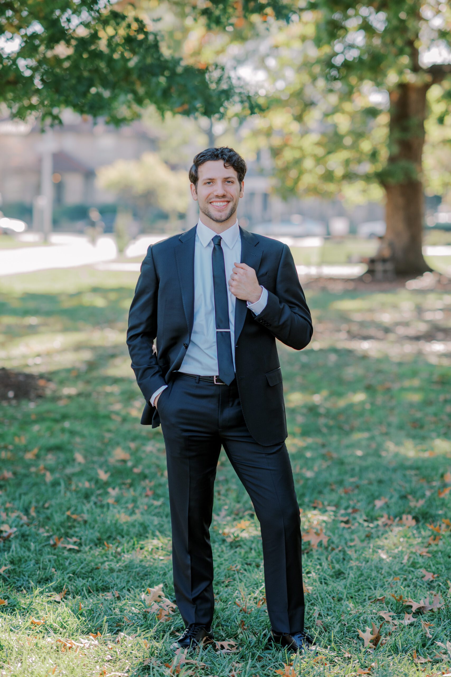 Solo photo of groom dressed in his suit, holding onto his jacket with one hand while his other hand is in his pocket