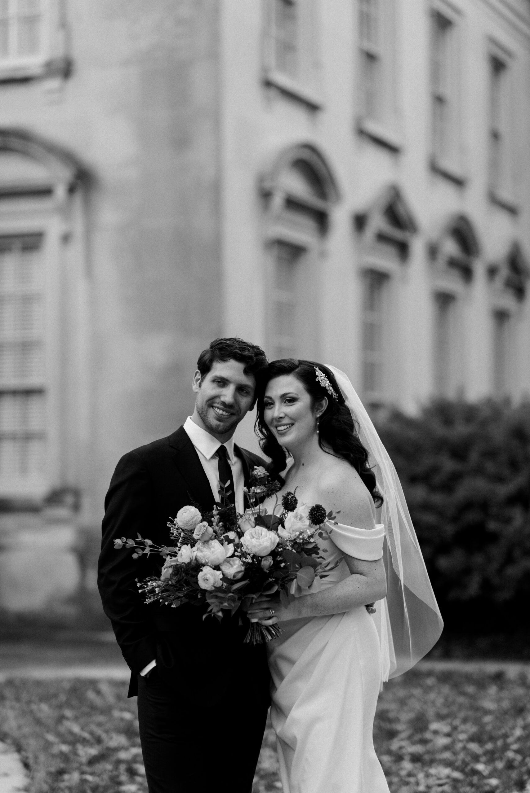 Black and white knees up image of bride and groom smiling with building in background