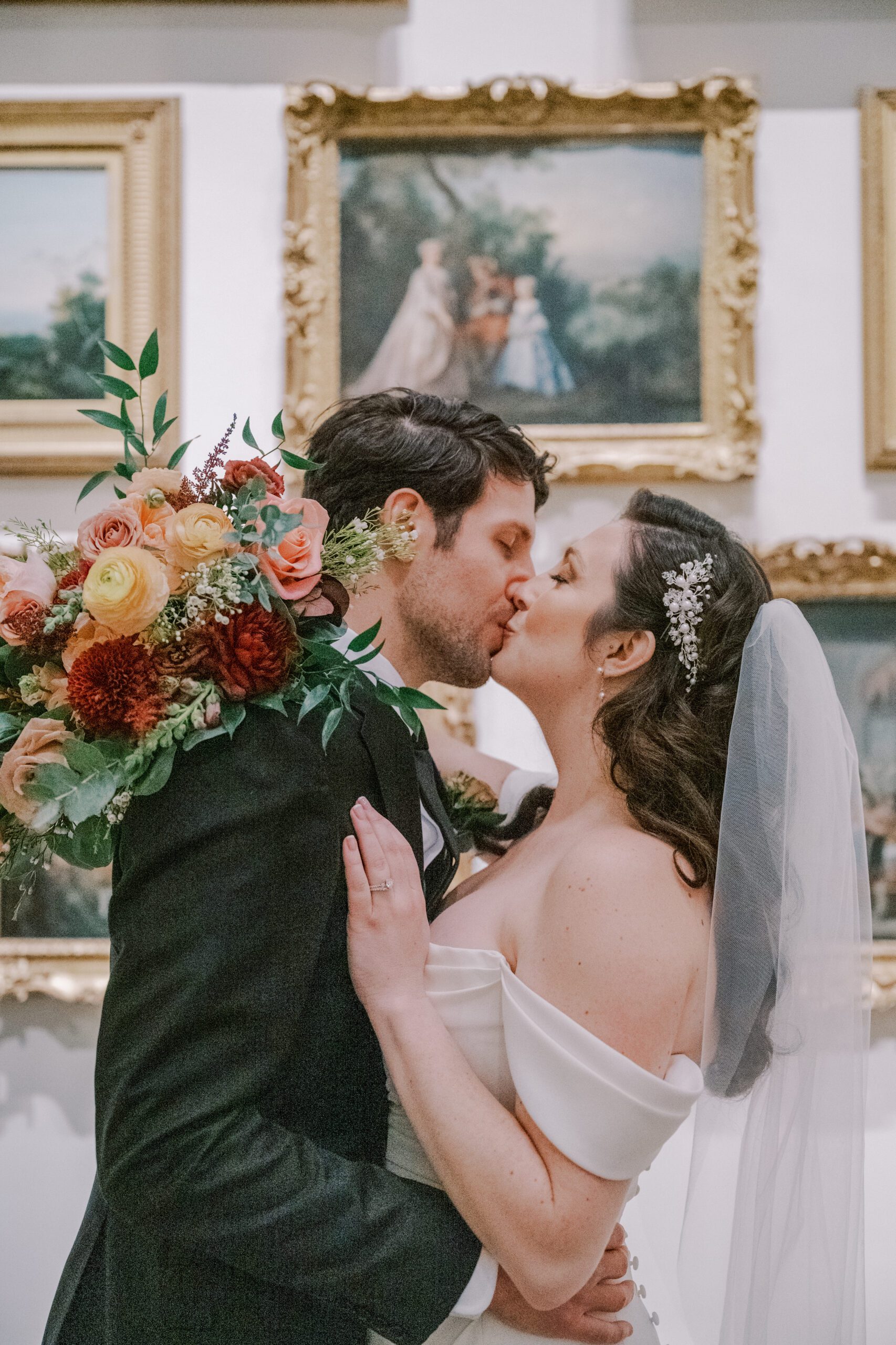Bride and groom kissing with paintings from the museum behind them