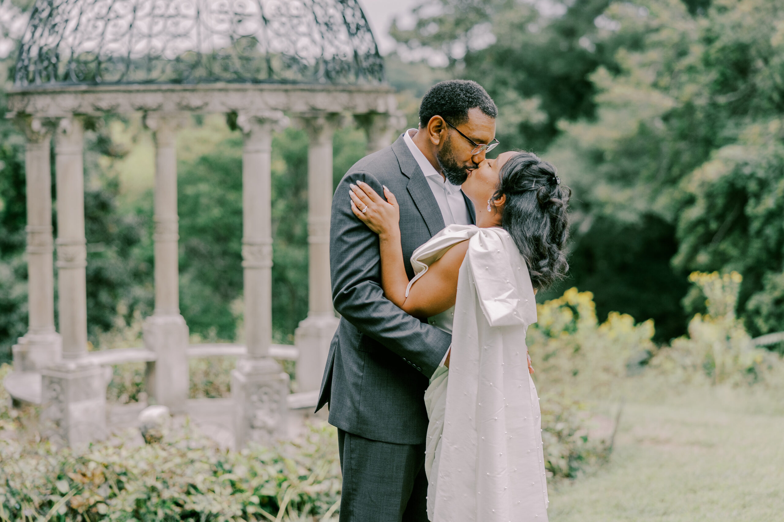 Engaged couple sharing a kiss with a gazebo in background at maymont