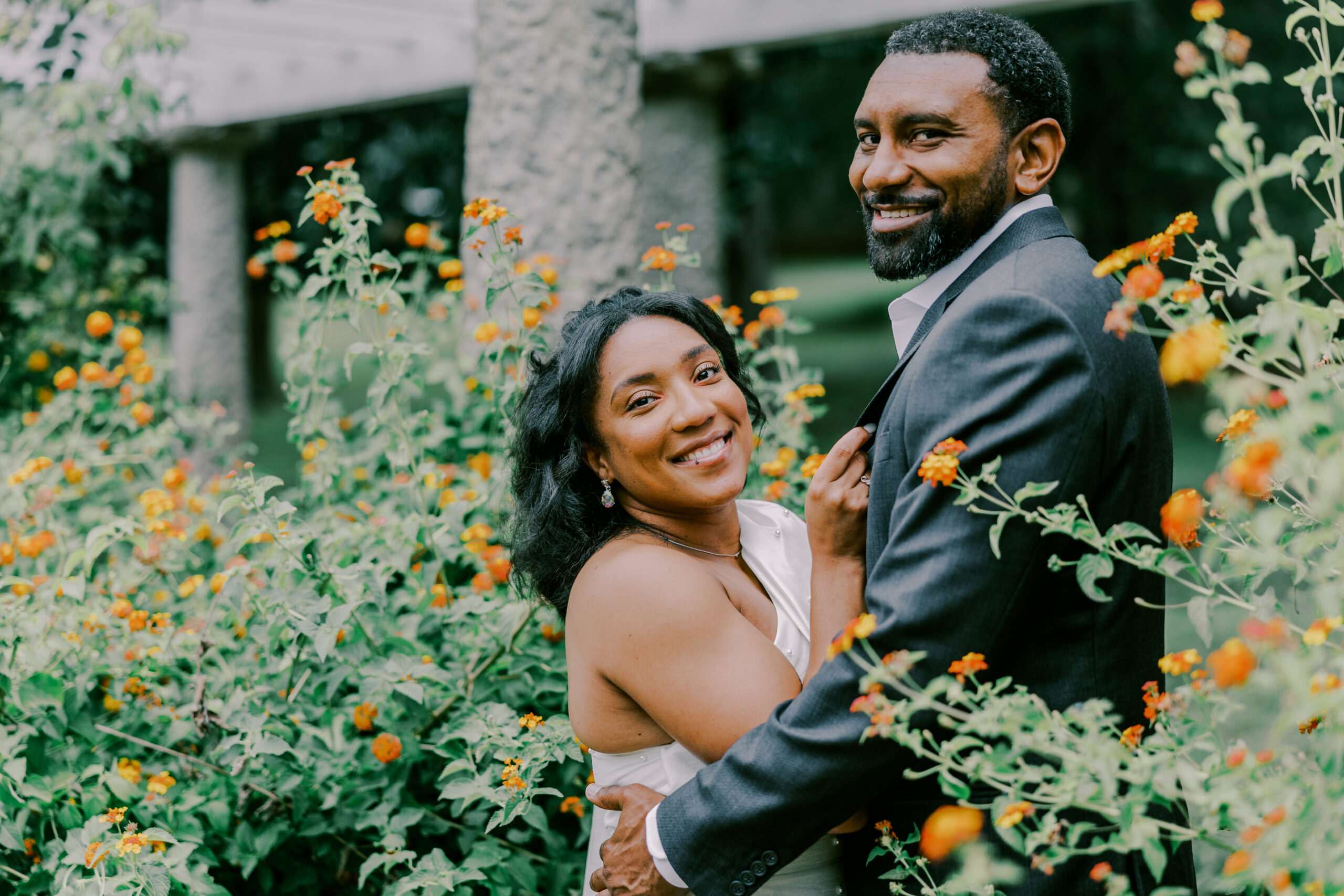 Couple standing with flower bushes on either side with orange flowers at maymont park