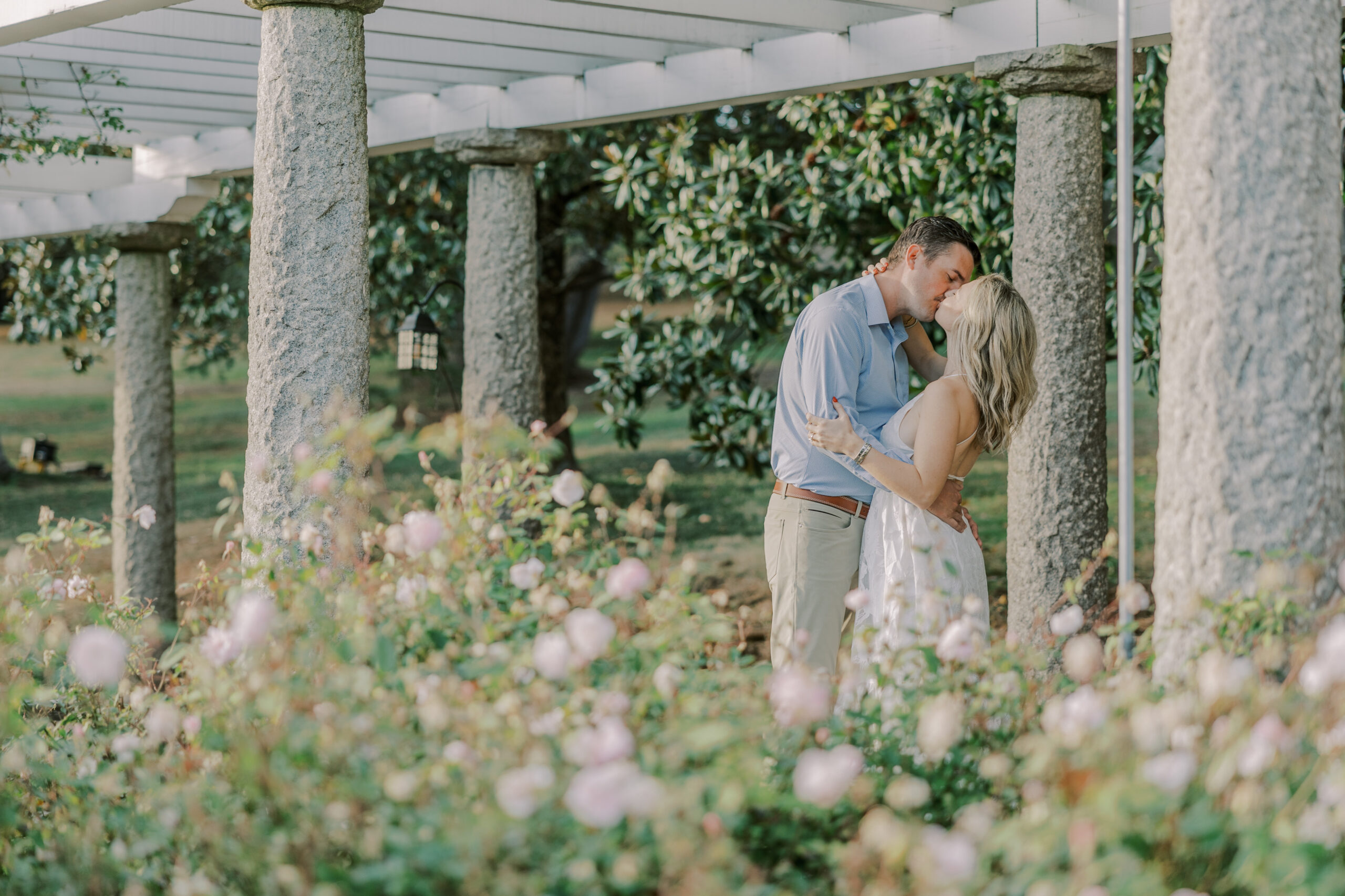 Man and woman kissing with stone columns, flowers and greenery around them