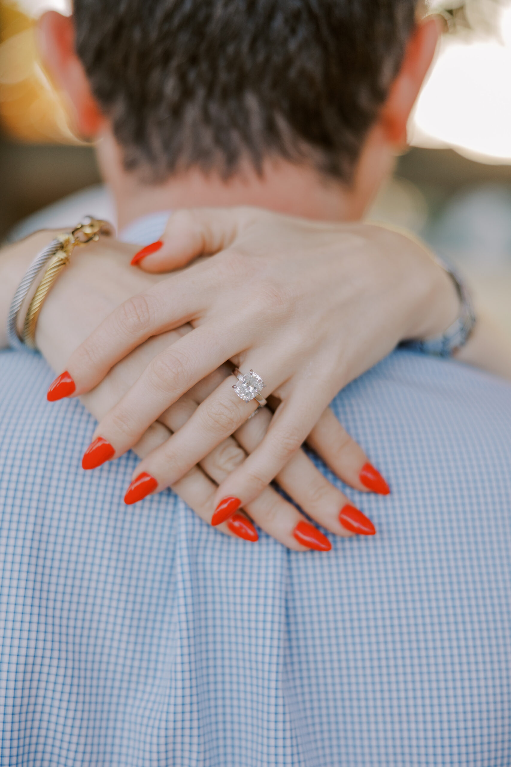 close up photo of woman's hands while she is embracing her fiance, her nails are red and she has a gold and diamond engagement ring on her finger