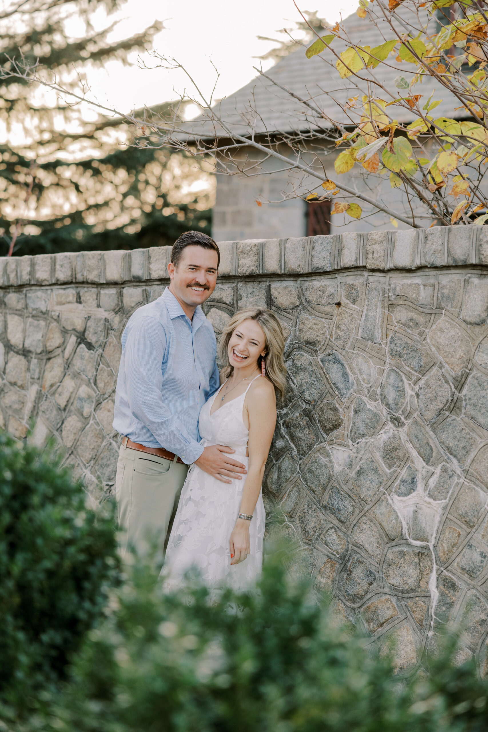 photo of man and woman leaning against stone wall smiling at camera at maymont