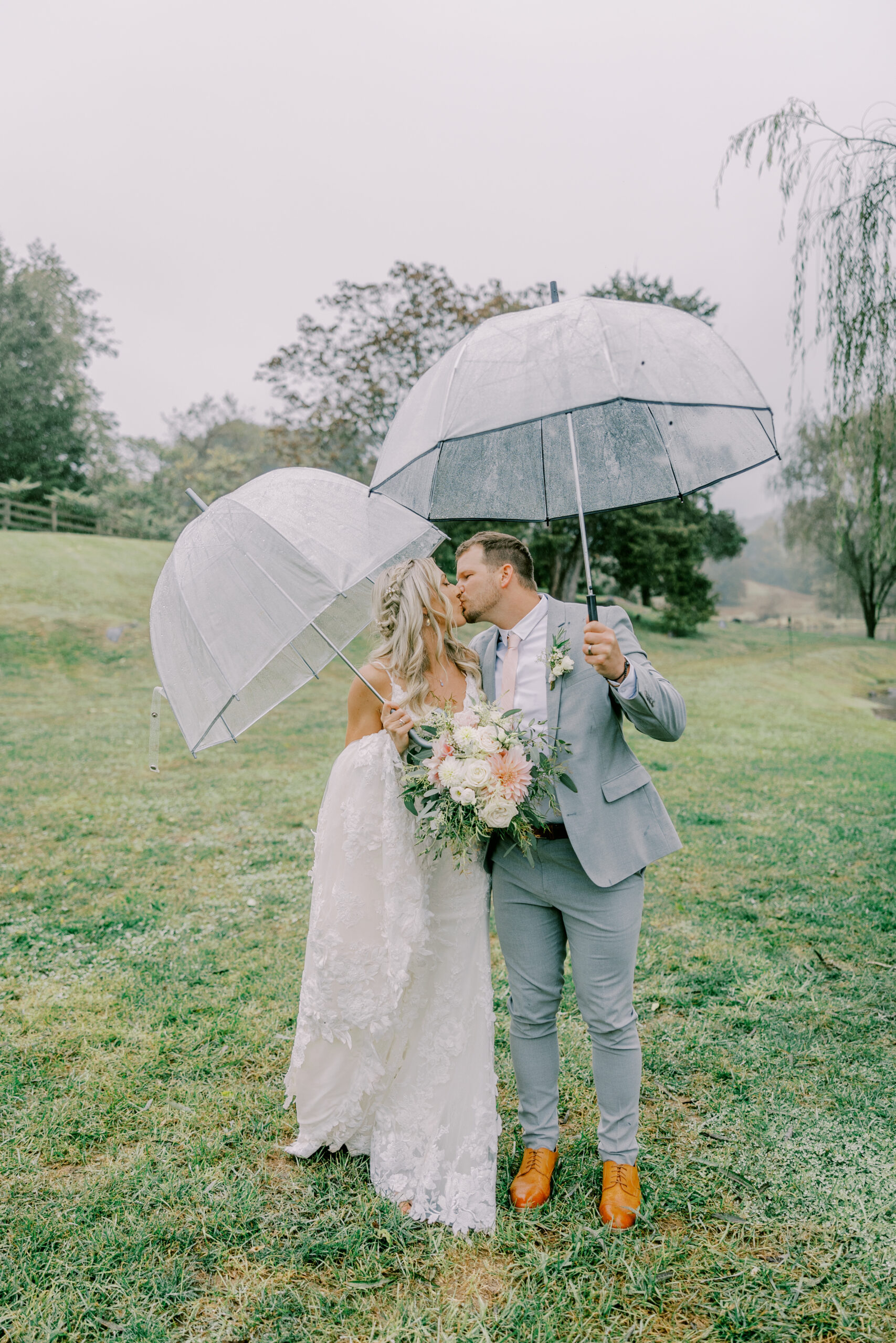 bride and groom pose for a kiss under umbrellas during their rainy wedding day